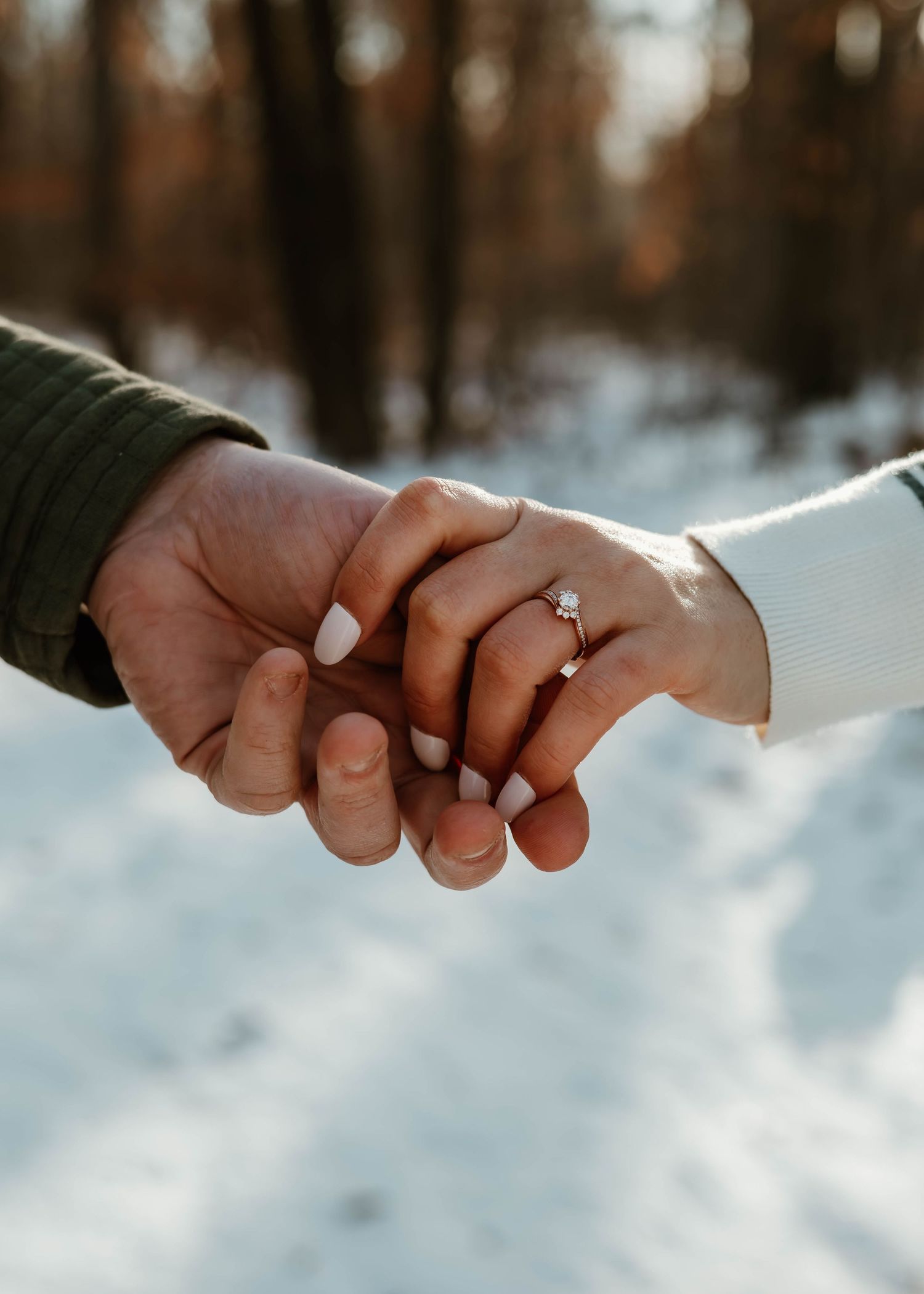 Close-up of hands reaching out to hold each other against a snowy winter forest backdrop.
