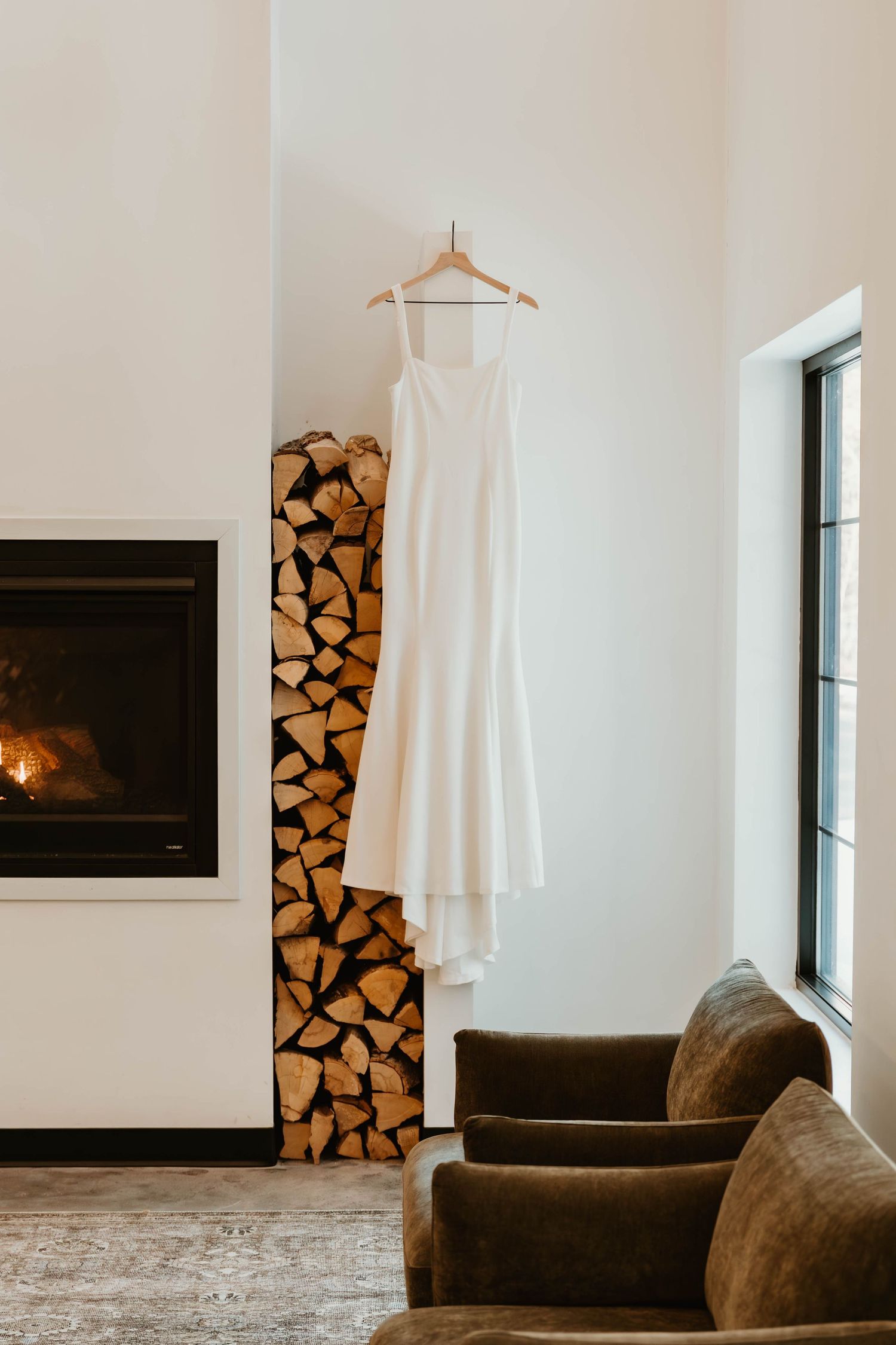 Modern living room interior with brown armchair, firewood storage, and white walls.