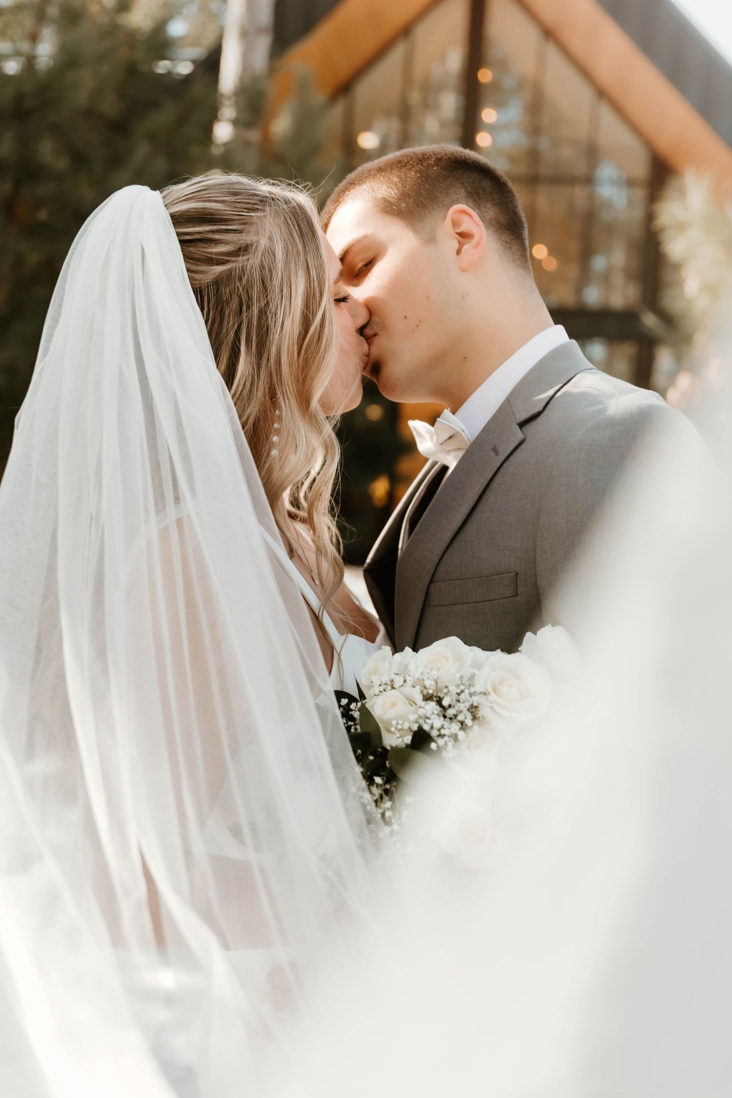 Tender wedding moment captured through delicate white veil in winter setting.