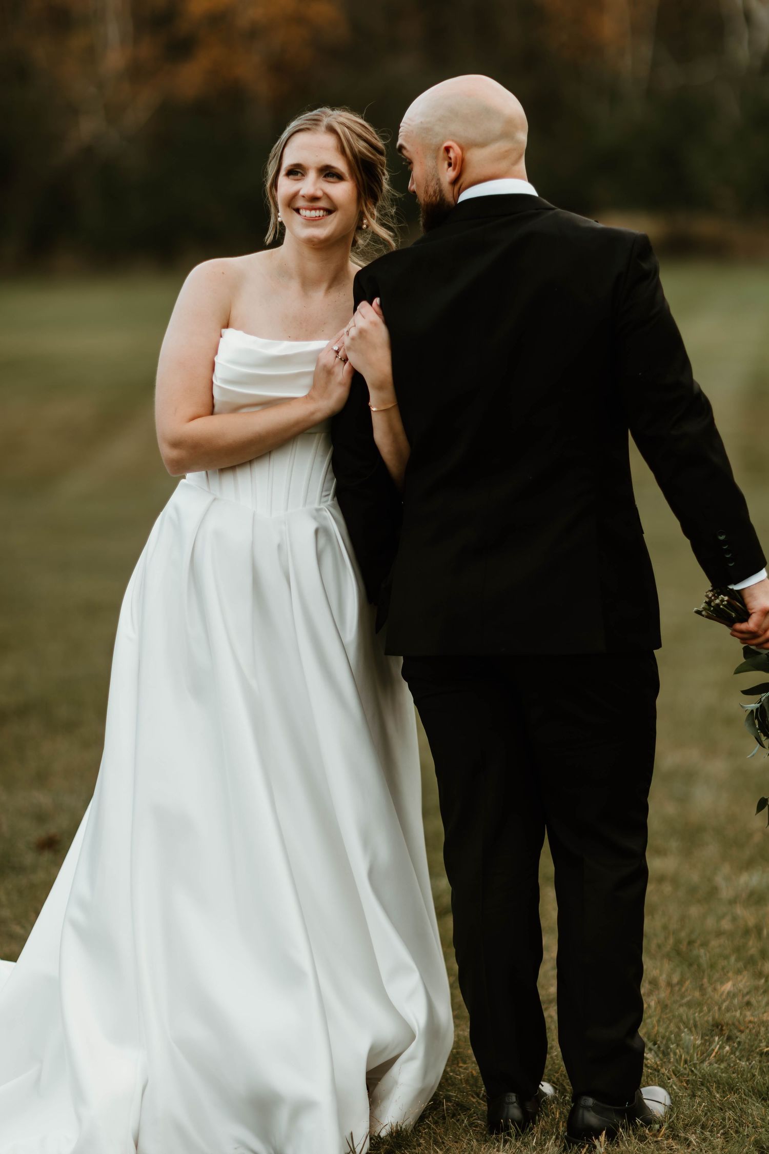 Wedding couple walking together outdoors with the bride in a flowing white gown against an autumn backdrop.