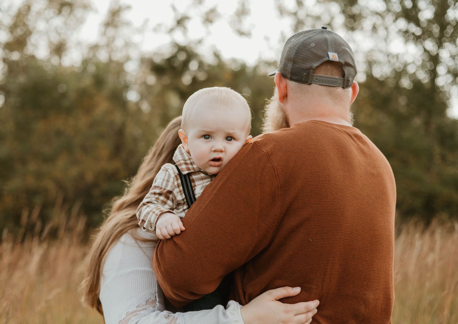 A tender moment between parent and baby in a golden-lit field during sunset.