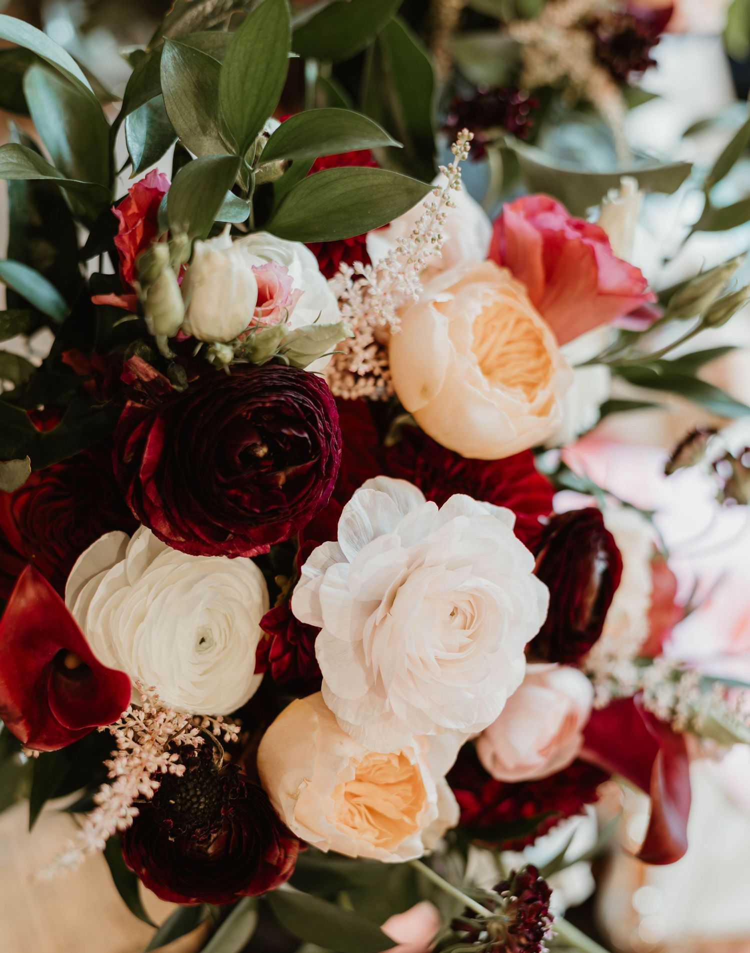 A romantic floral arrangement featuring deep burgundy and blush pink roses with delicate greenery and foliage.