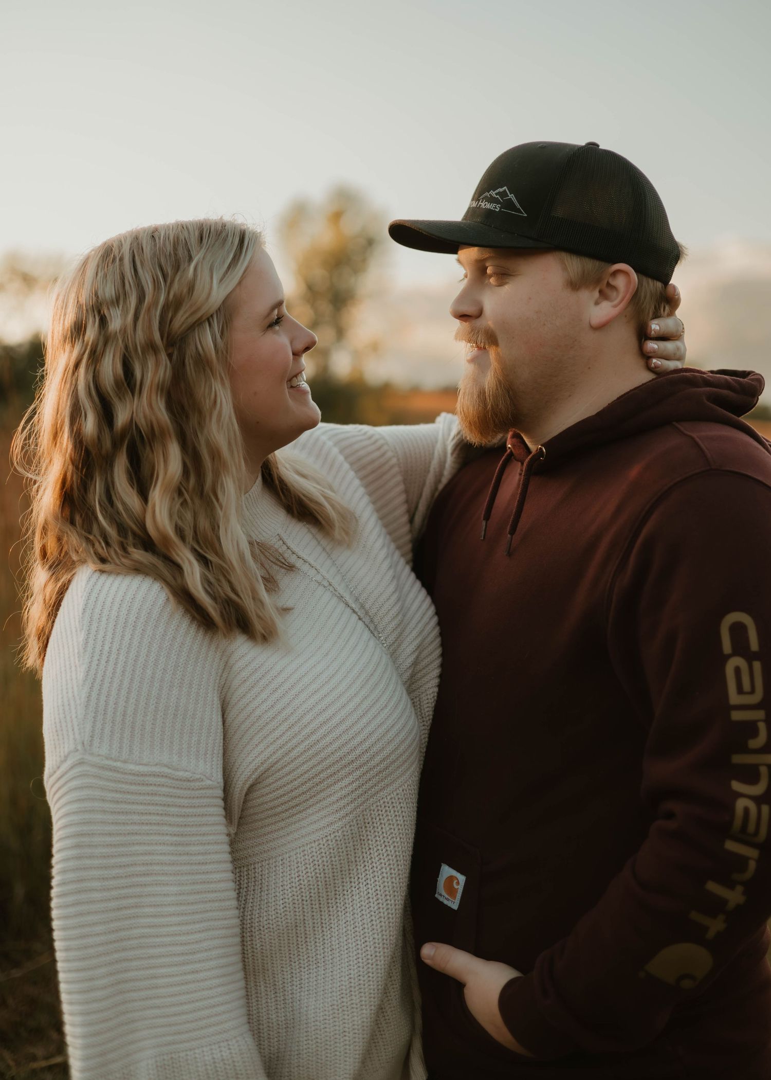 A couple shares intimate moments at sunset while wearing casual attire including a white sweater and brown jacket.