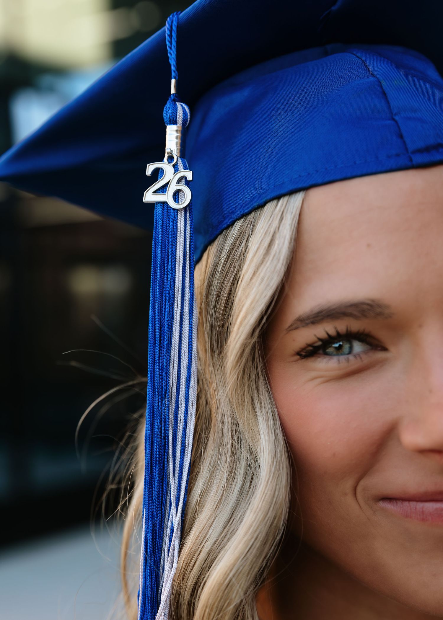 Young woman smiling in blue graduation cap with '26' charm and tassel, celebrating her upcoming graduation.