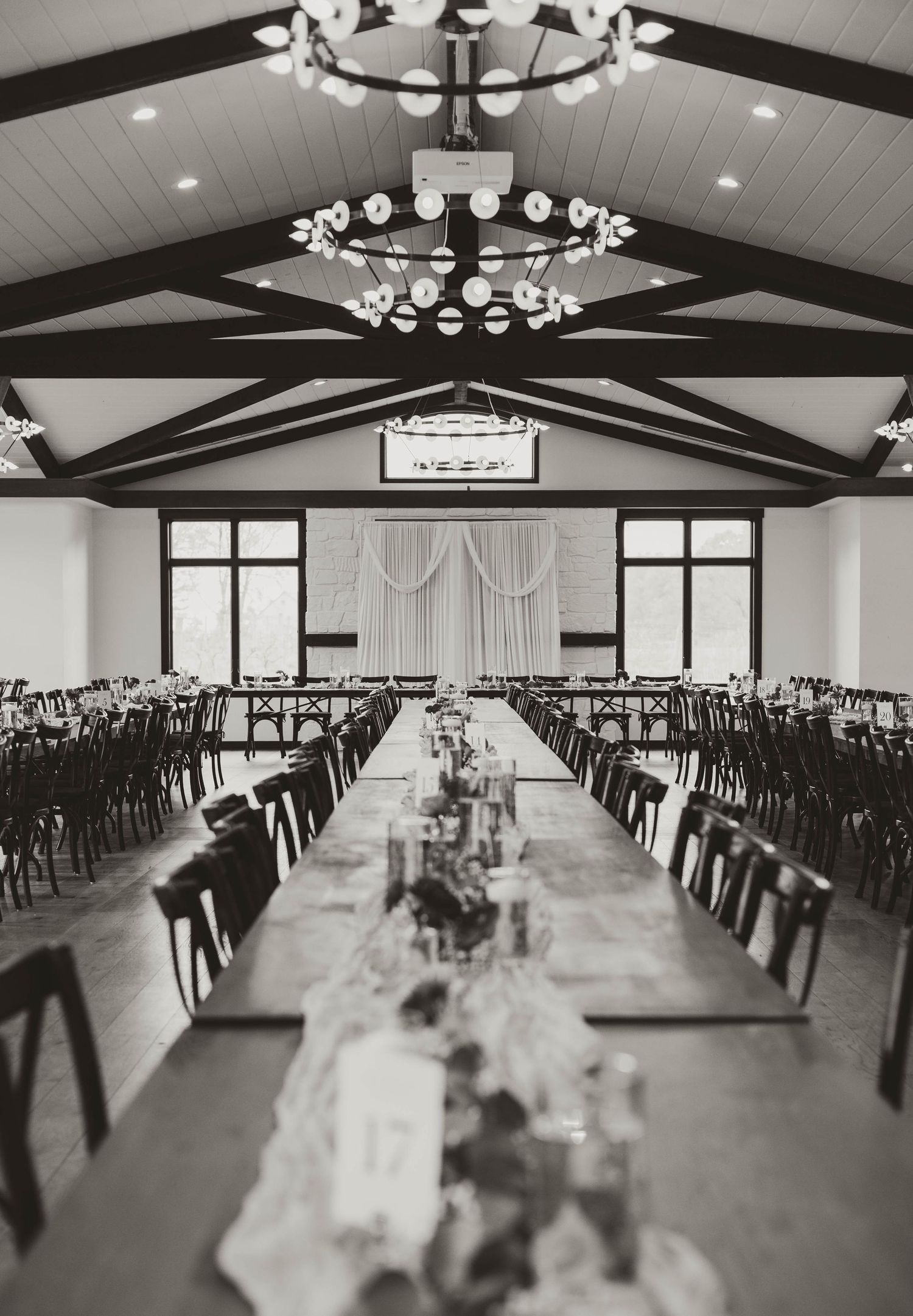 Wedding reception hall with vaulted ceiling, chandeliers and rows of tables set for celebration.