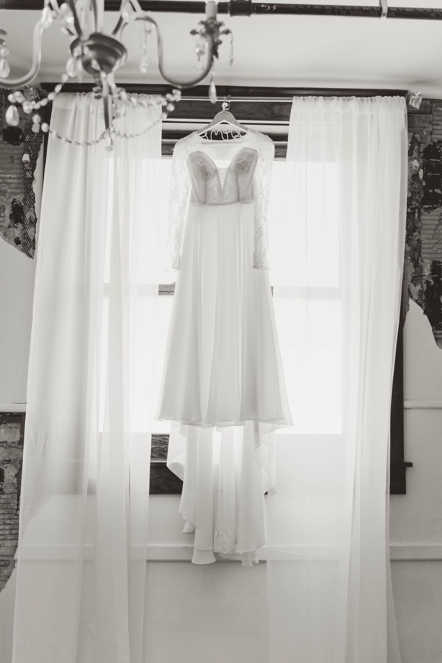 A row of white vintage dresses and garments hanging on hangers against a white wall with natural lighting.