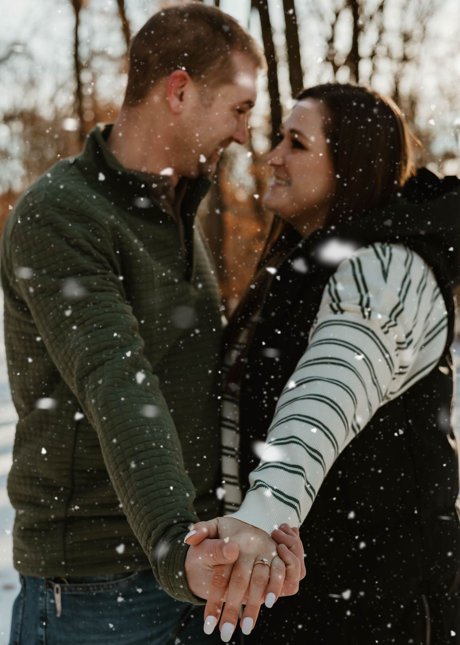 A couple shares an intimate moment in the falling snow while holding hands and leaning in close to each other.
