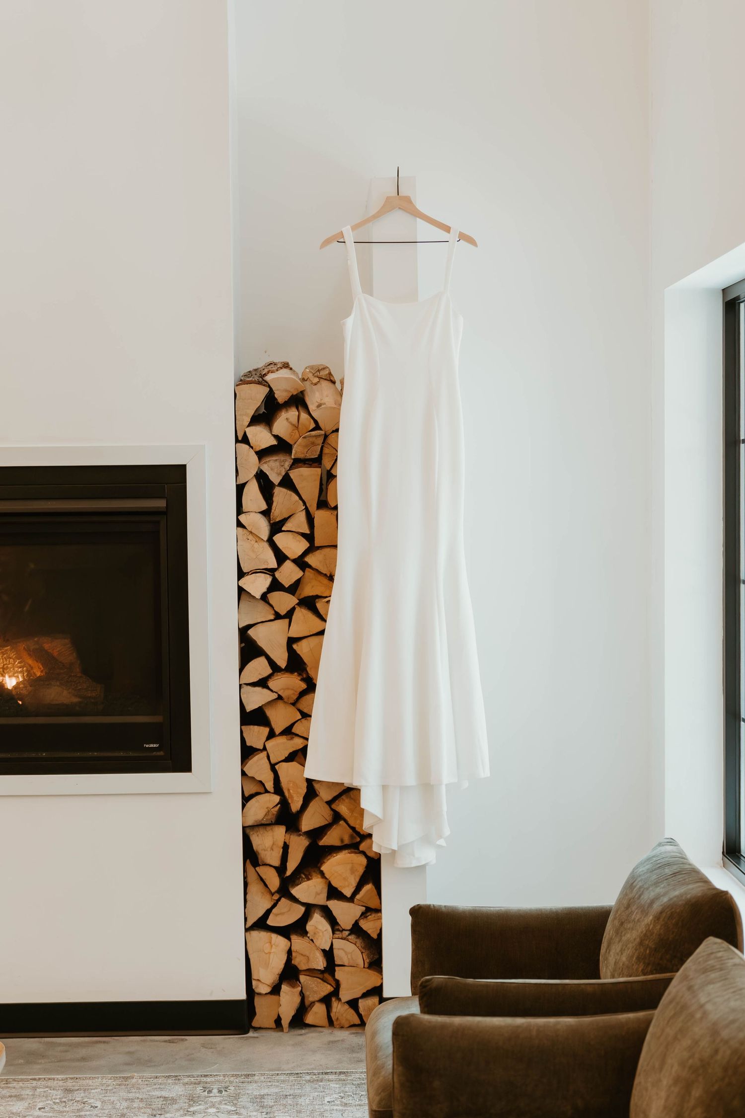 Minimalist white interior with stacked firewood, dark sofa, and white dress on display.