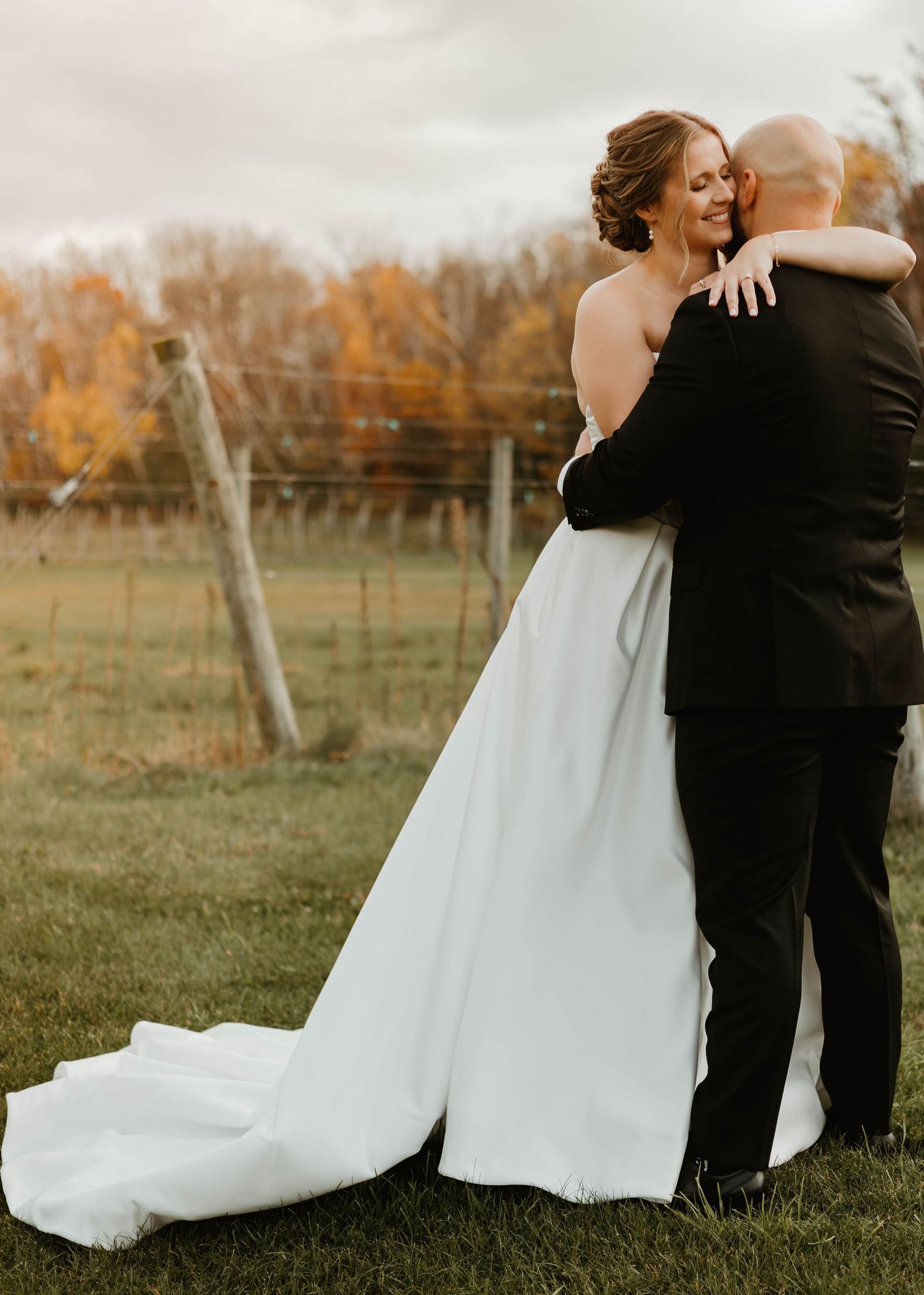 Wedding couple embracing in outdoor field with autumn colors in background.