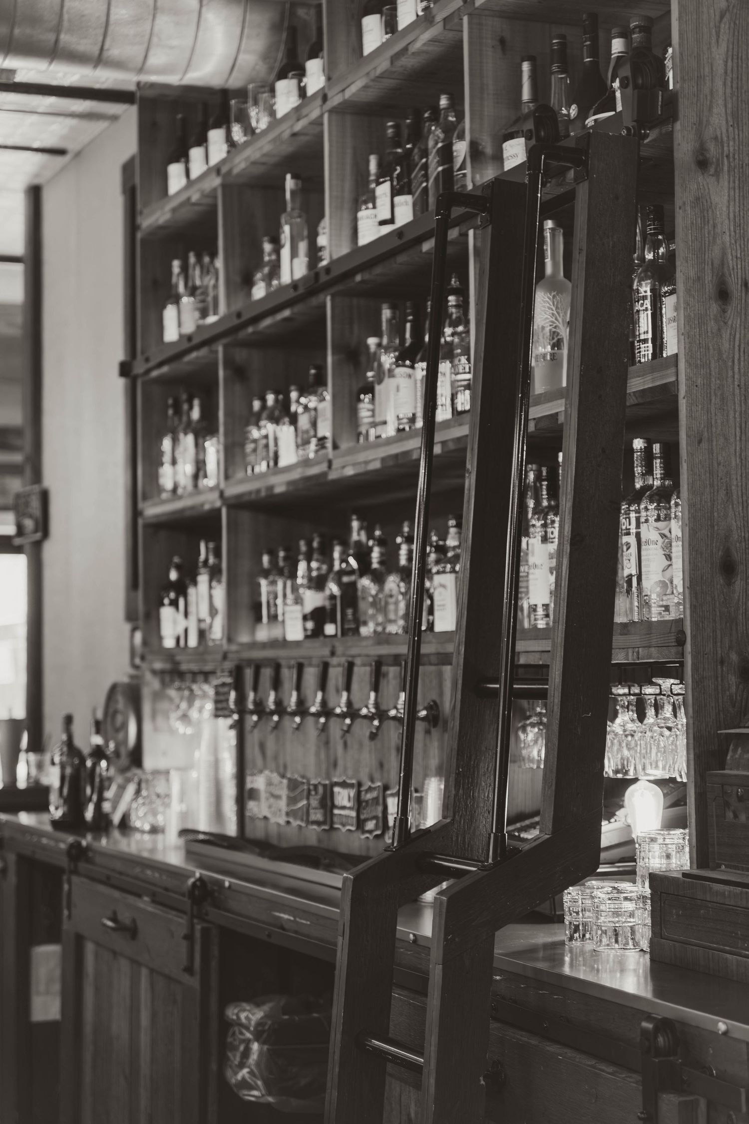 Vintage wooden bar shelving stocked with glass bottles and liquor in an industrial-style setting.