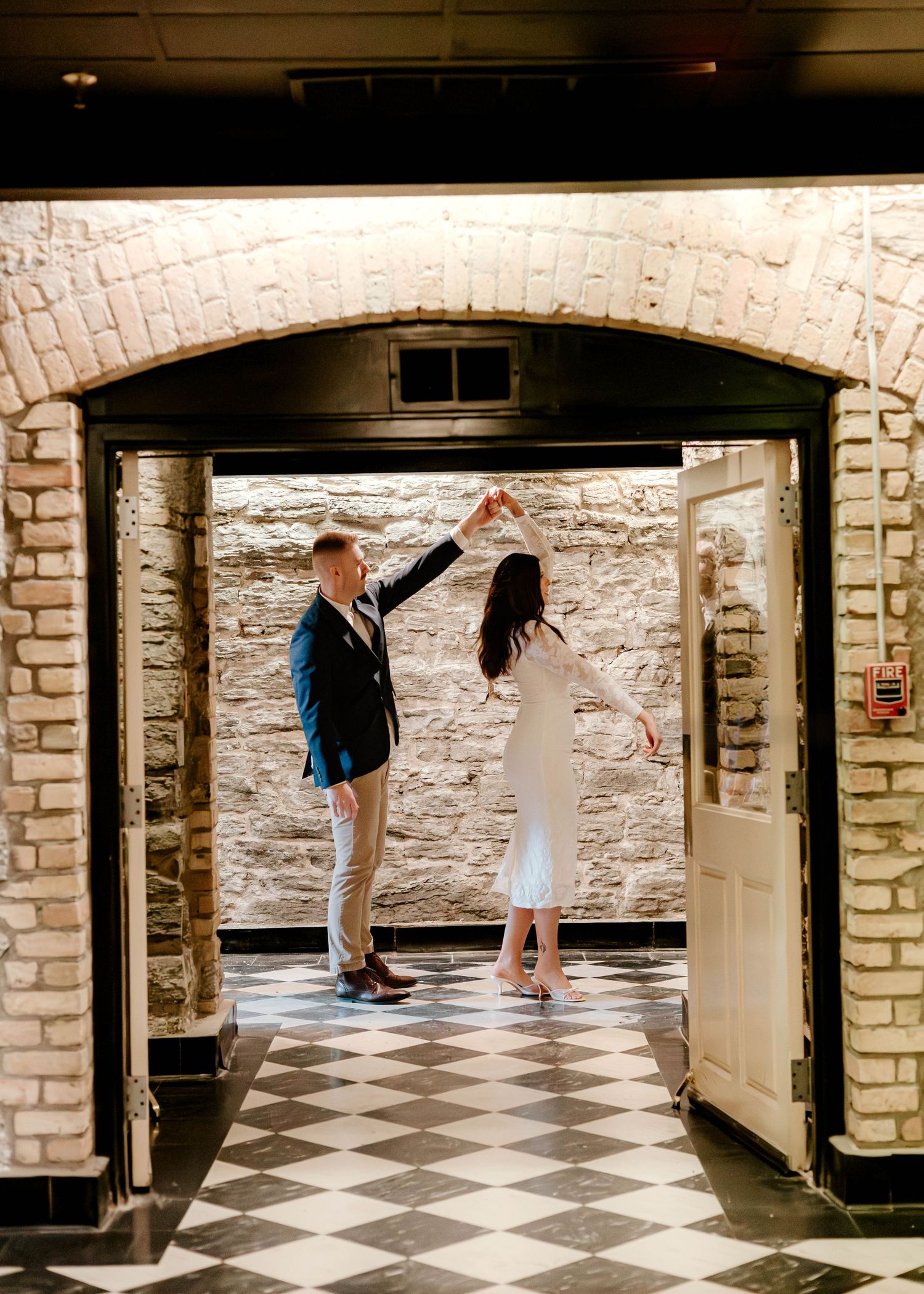 A couple walks through a historic stone basement hallway with black and white checkered floors.