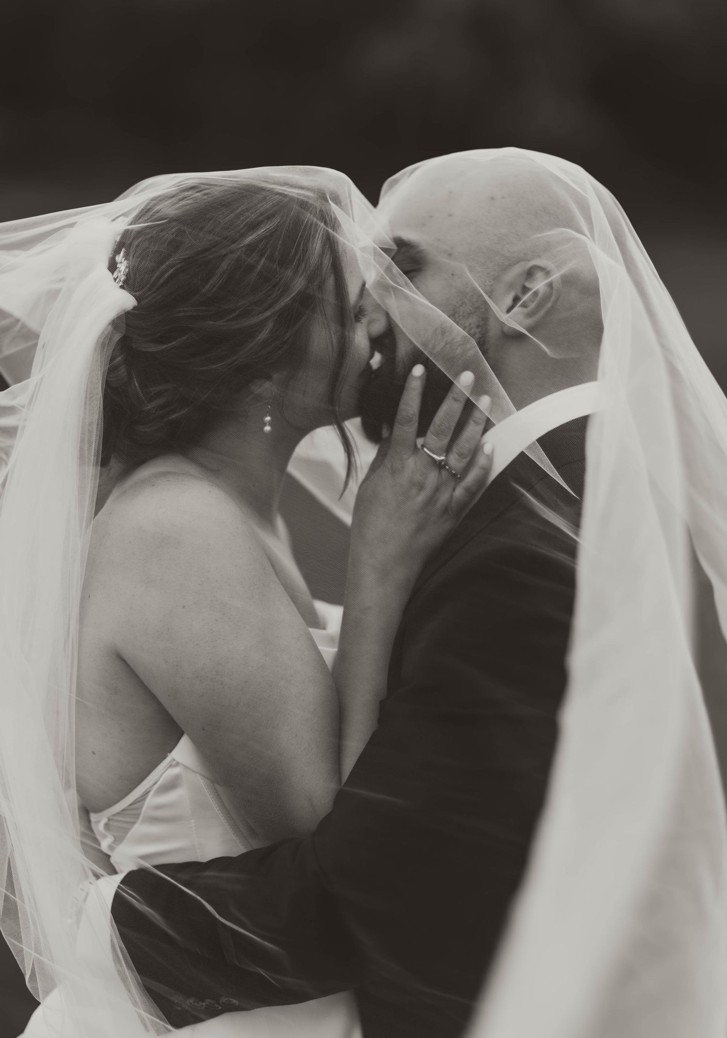 Romantic wedding kiss under flowing white veil in black and white.