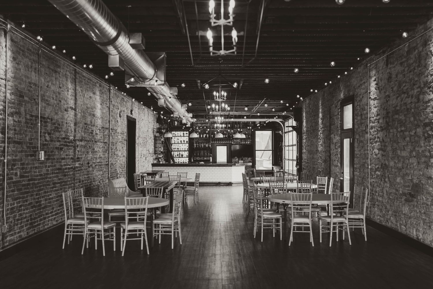Black and white photo of an empty industrial event space with brick walls and tables.