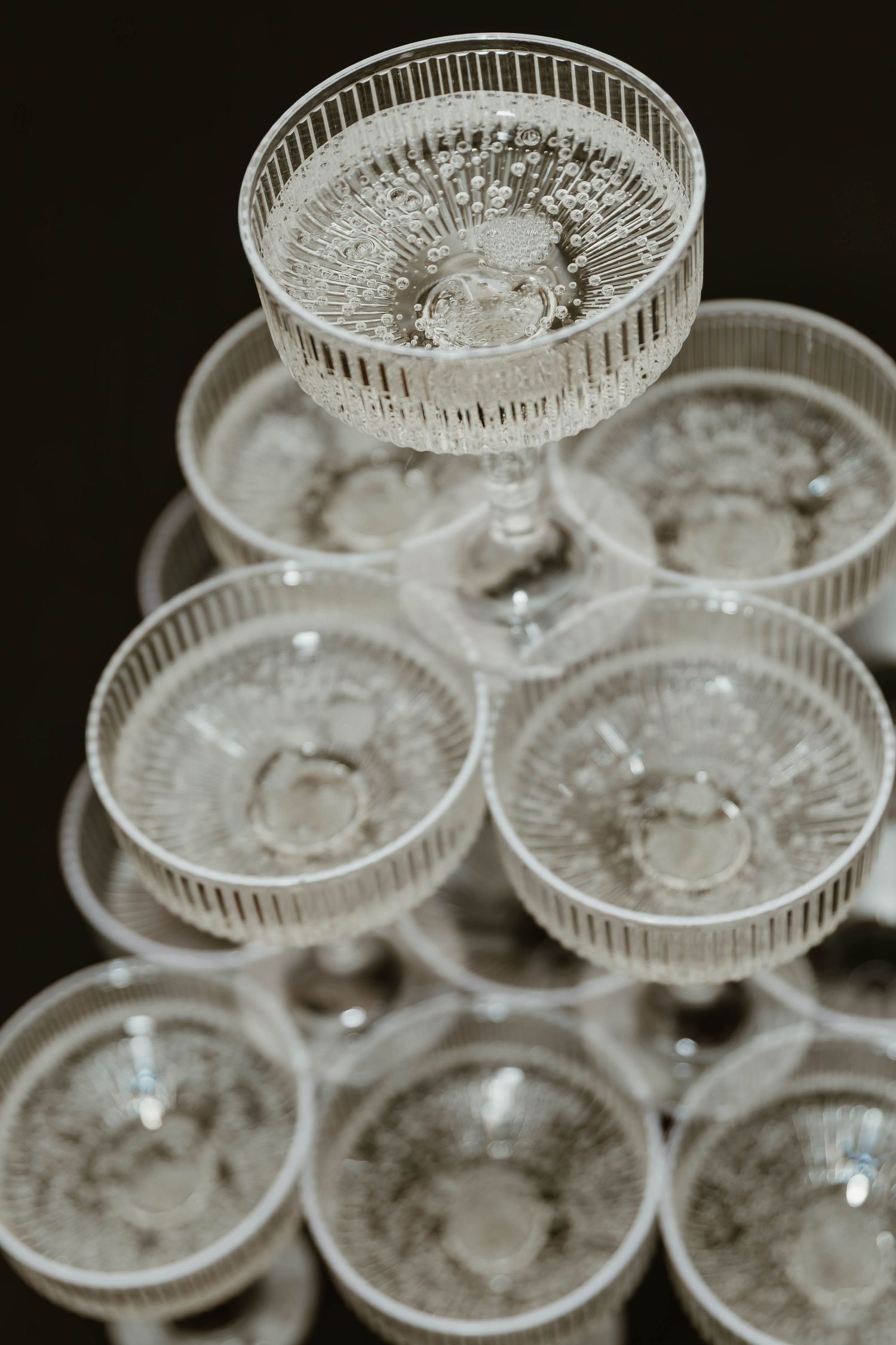 Vintage cut glass champagne coupes stacked in an elegant display on black.