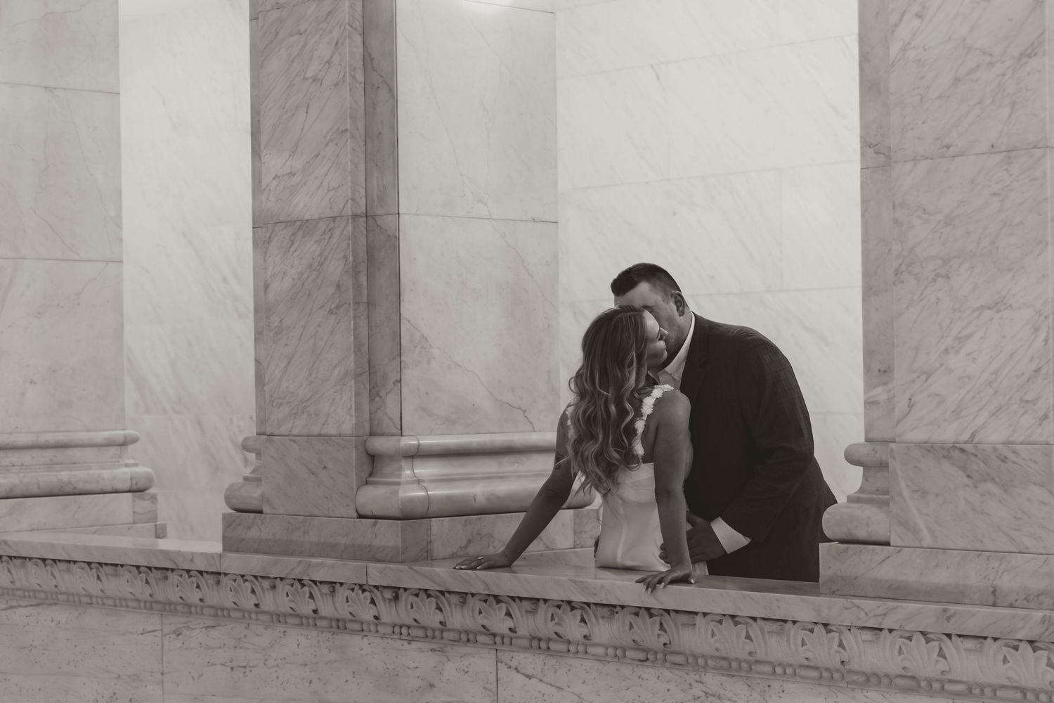 A romantic black and white photograph of a couple embracing near marble columns.