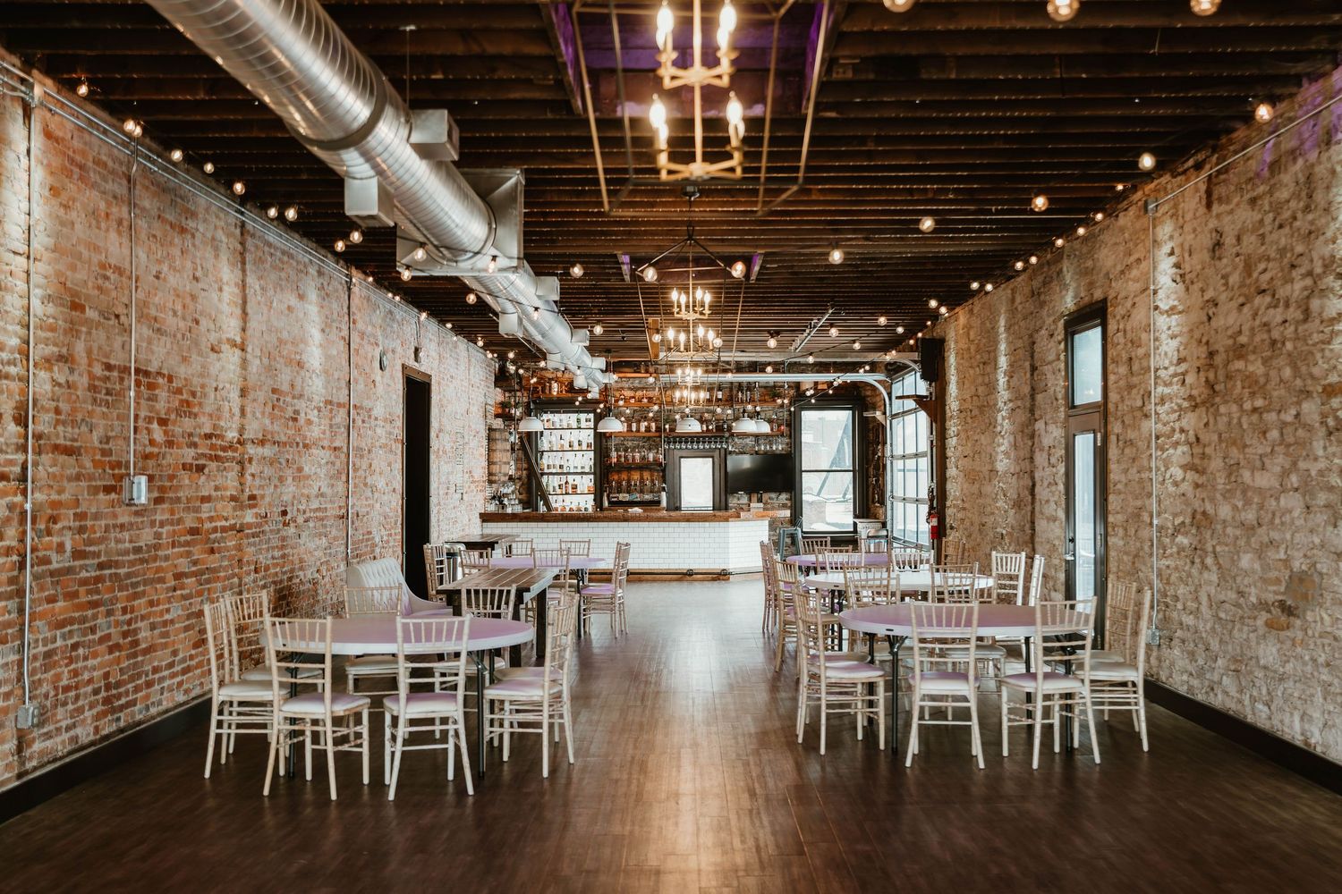 Rustic brick wall event venue with exposed beams, string lights, and white chairs arranged in rows for a ceremony at The 3 ten event Center.
