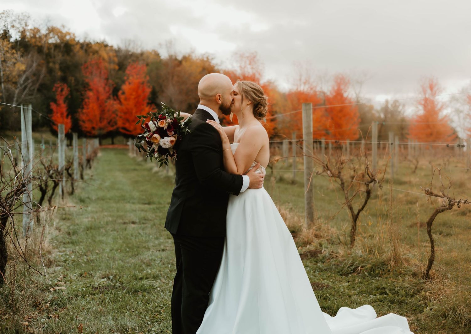 A romantic couple shares intimate moments in a vineyard with autumn foliage creating a warm backdrop.