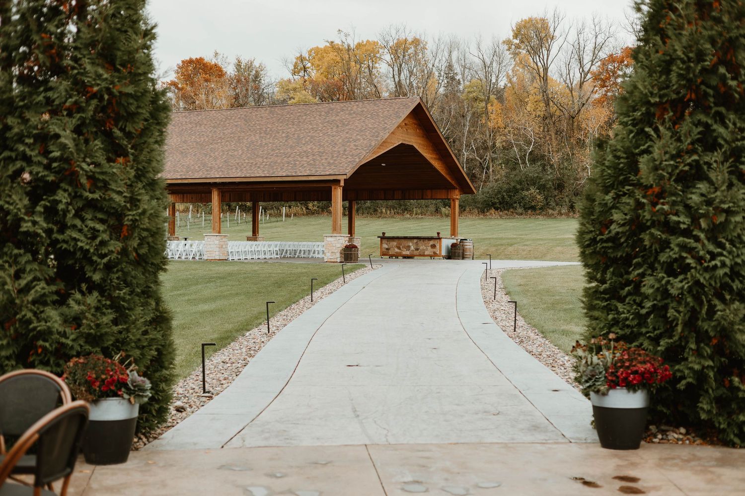 Landscaped walkway leading to a rustic venue with evergreen trees and red flowers.