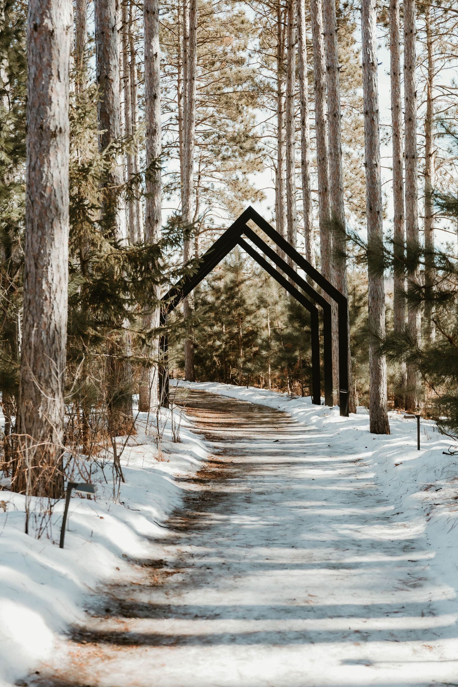 A snowy forest path with modern black triangular archways creating a geometric tunnel effect in winter.