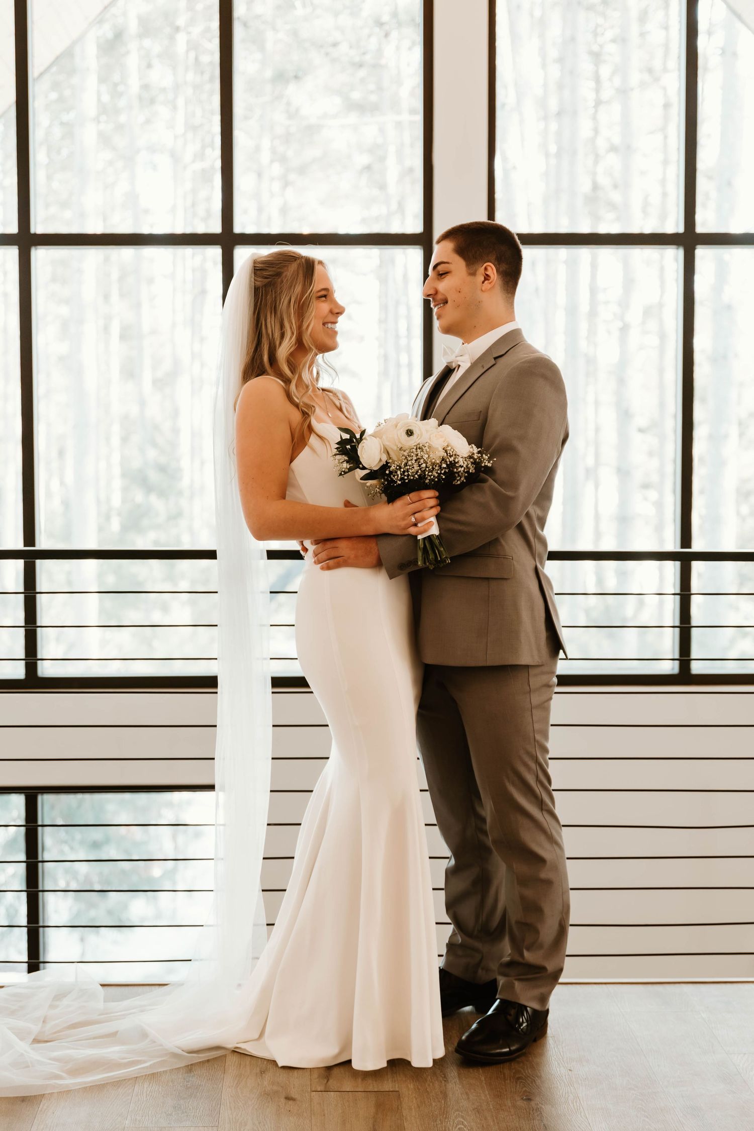 Newlyweds sharing an intimate moment in front of floor-to-ceiling windows.