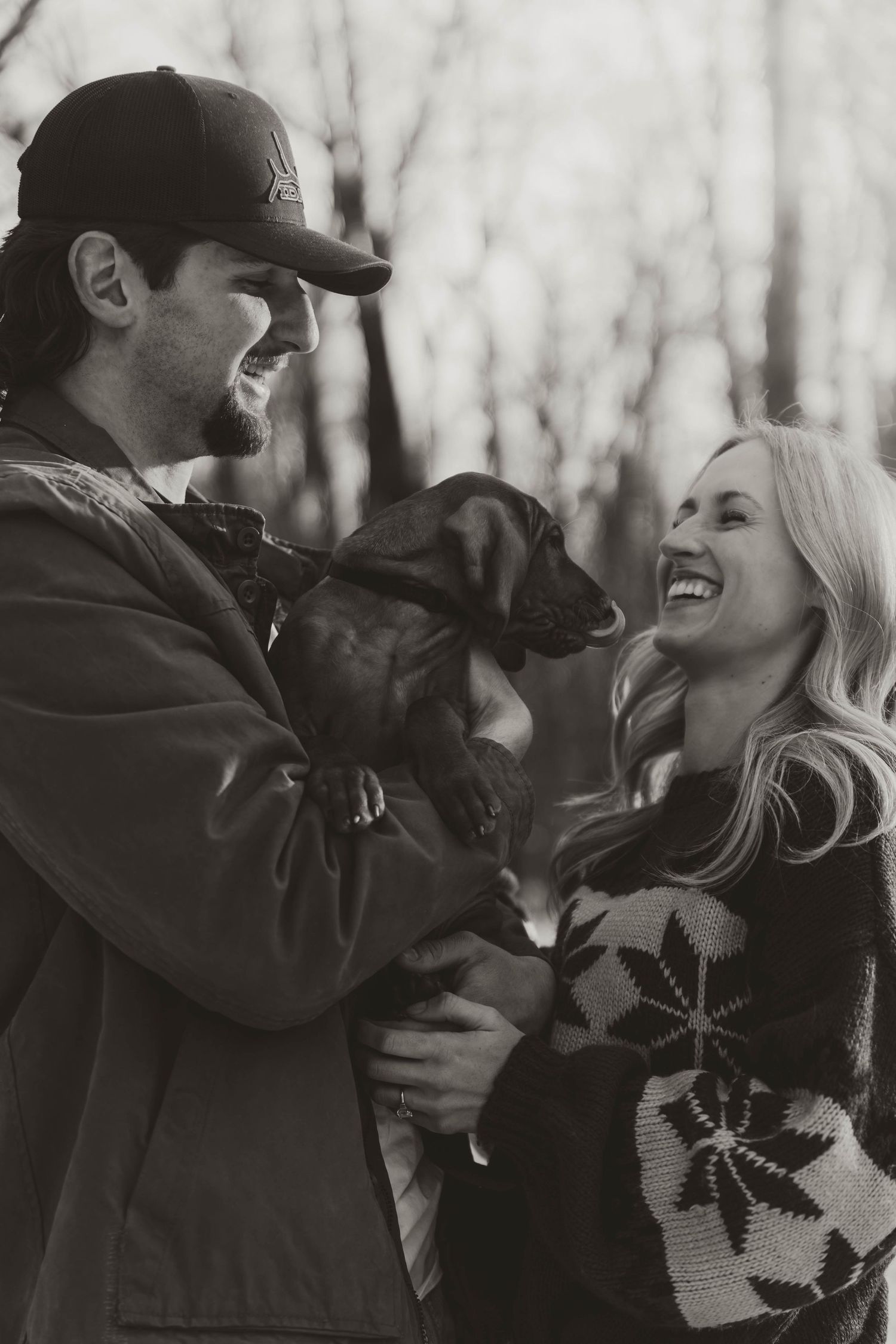 A couple shares a playful moment in black and white as their dog joins in the laughter and fun.