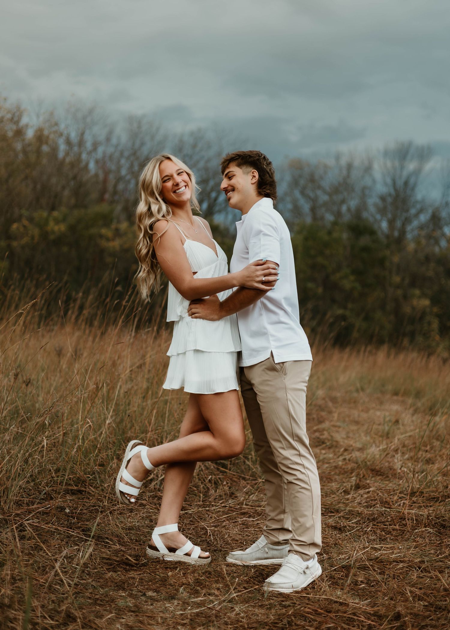 A couple in white outfits shares an intimate moment while dancing in a golden field at sunset.