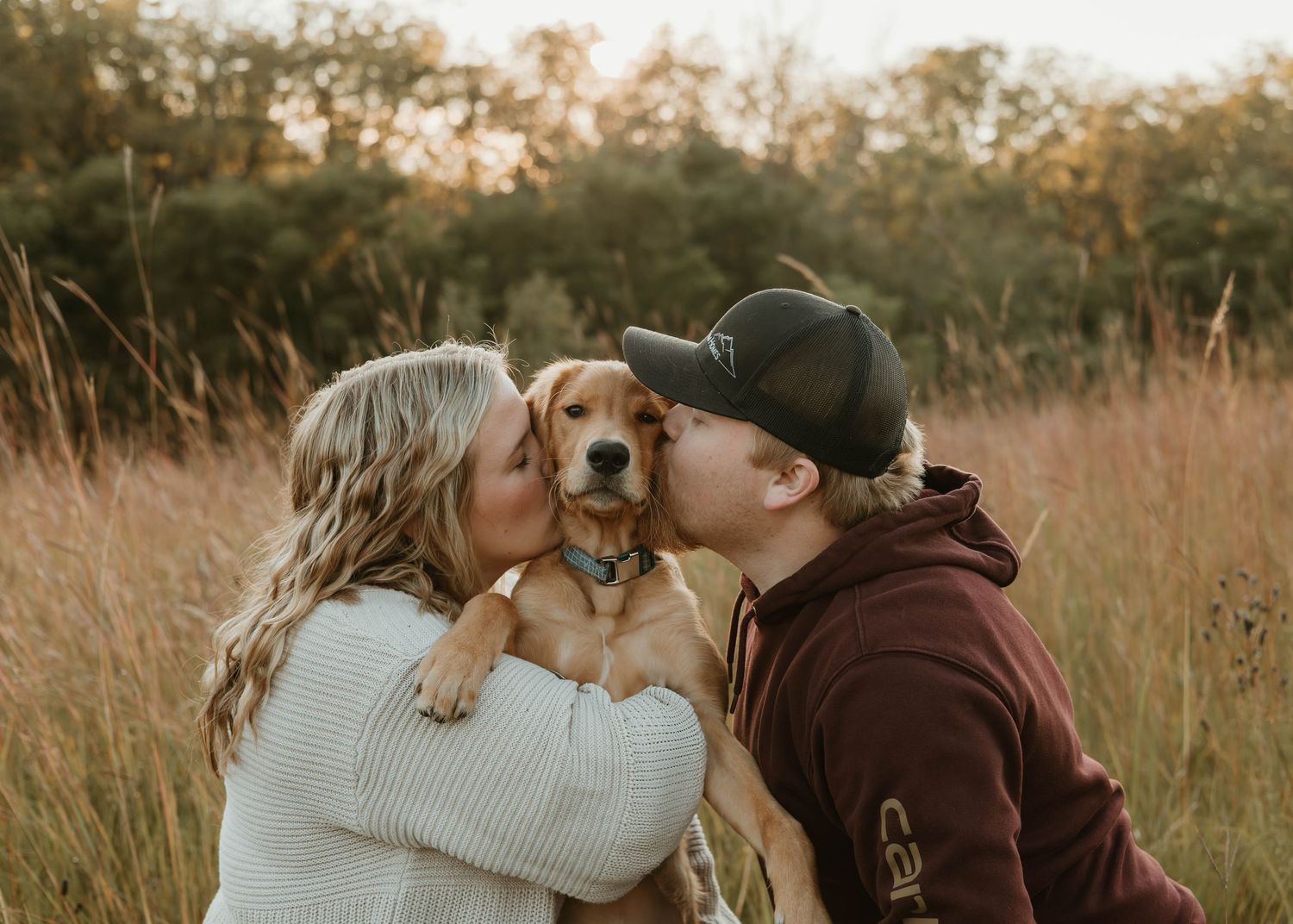 A romantic couple and their dog share tender moments in a golden sunlit field during sunset.
