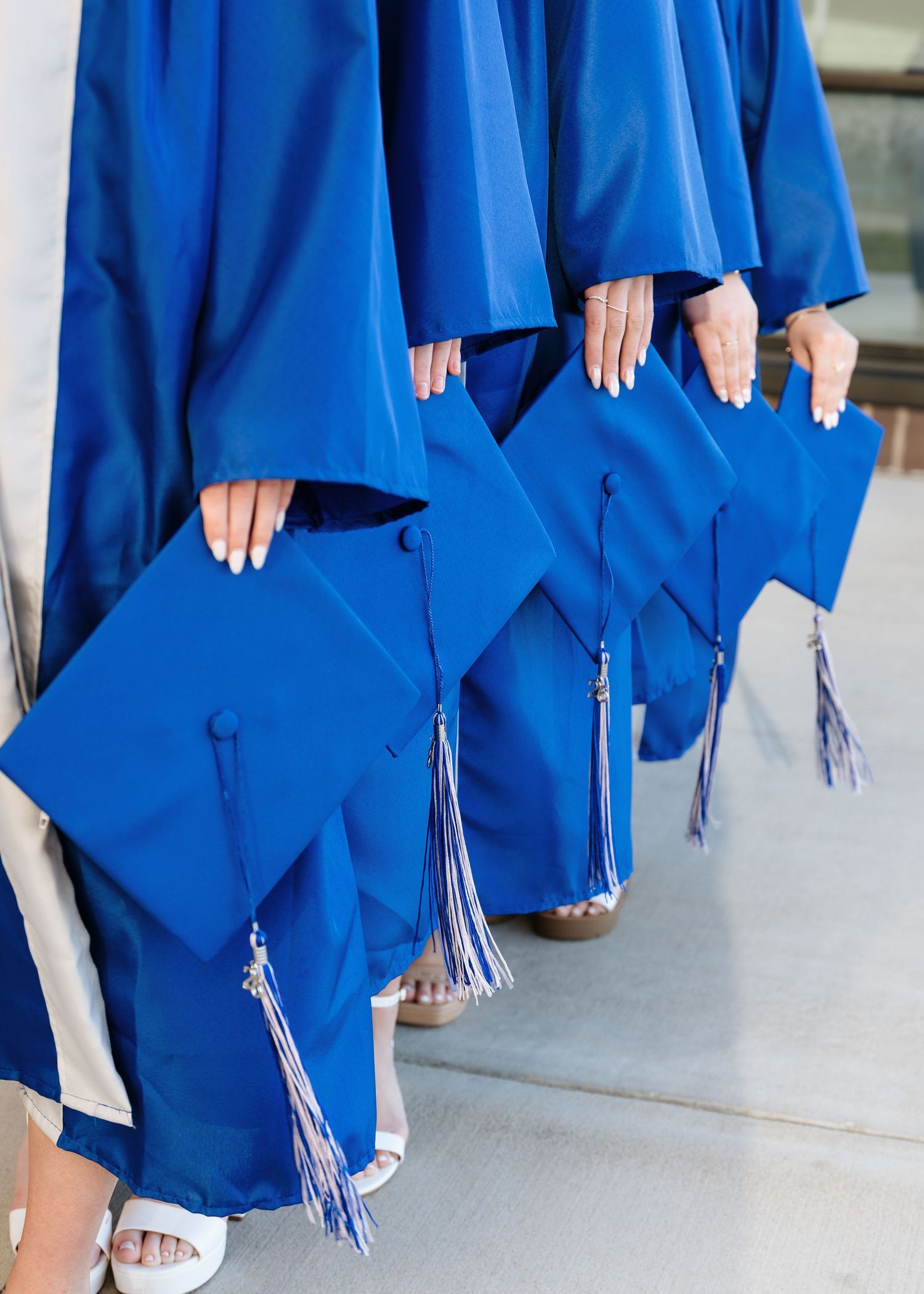 A row of graduates in royal blue caps and gowns holding their mortarboards with blue tassels at a graduation ceremony.