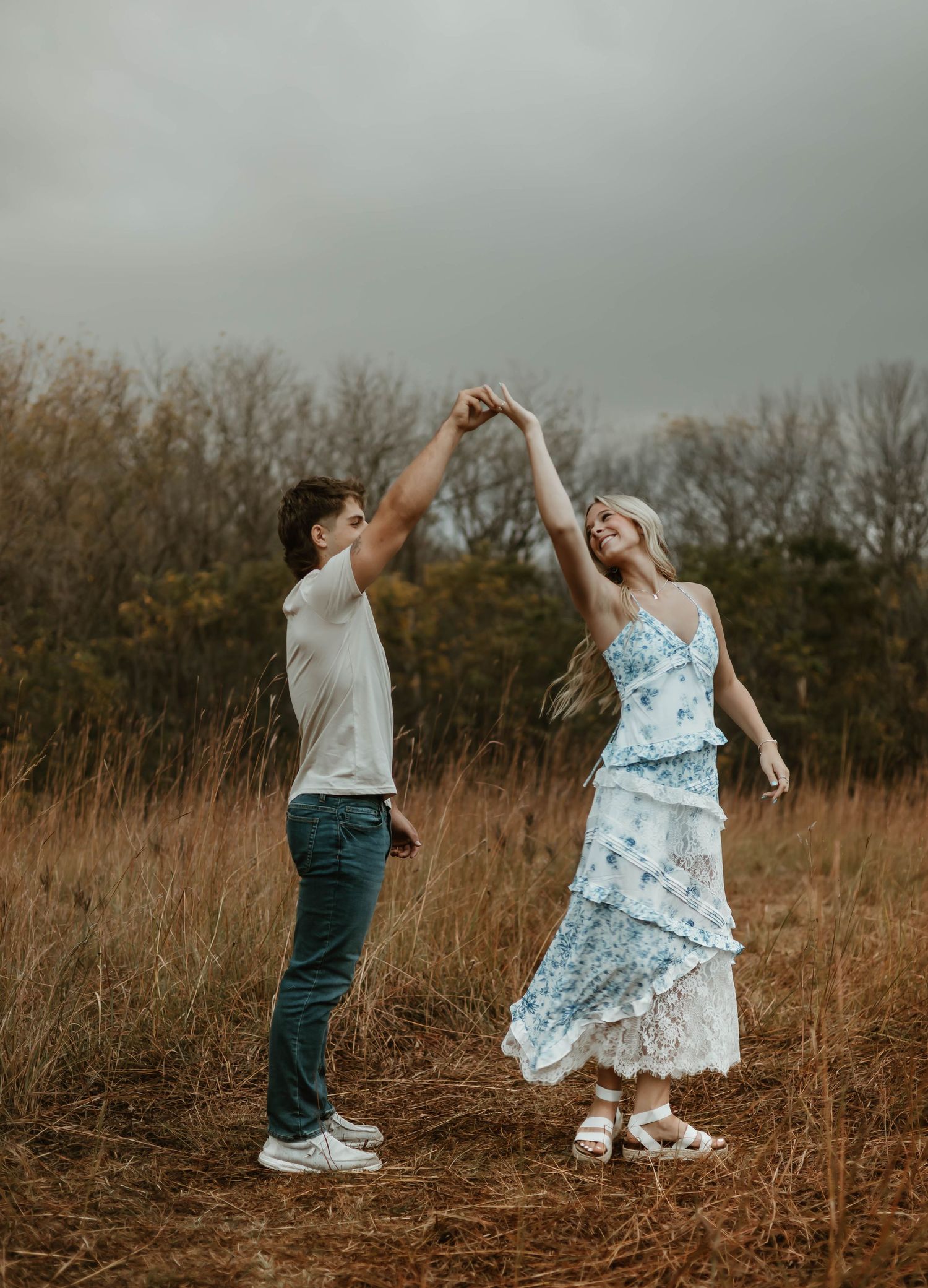 A couple dances together in a golden field at sunset with tall grass and trees in the background.