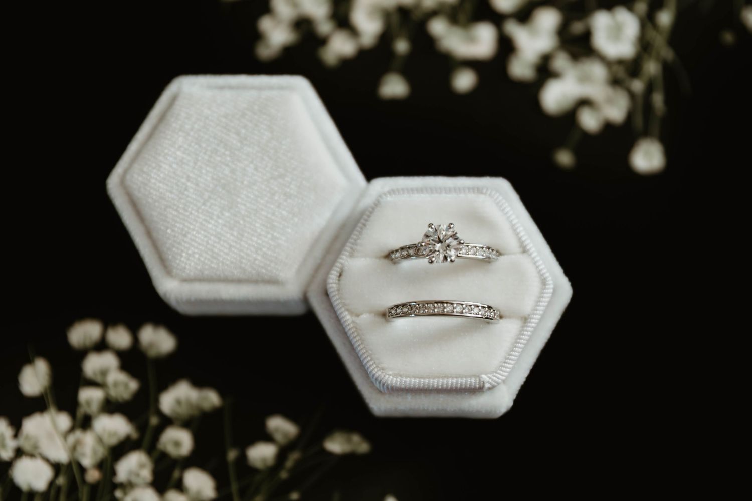 Two elegant wedding rings displayed in white hexagonal velvet ring boxes with delicate floral decor.