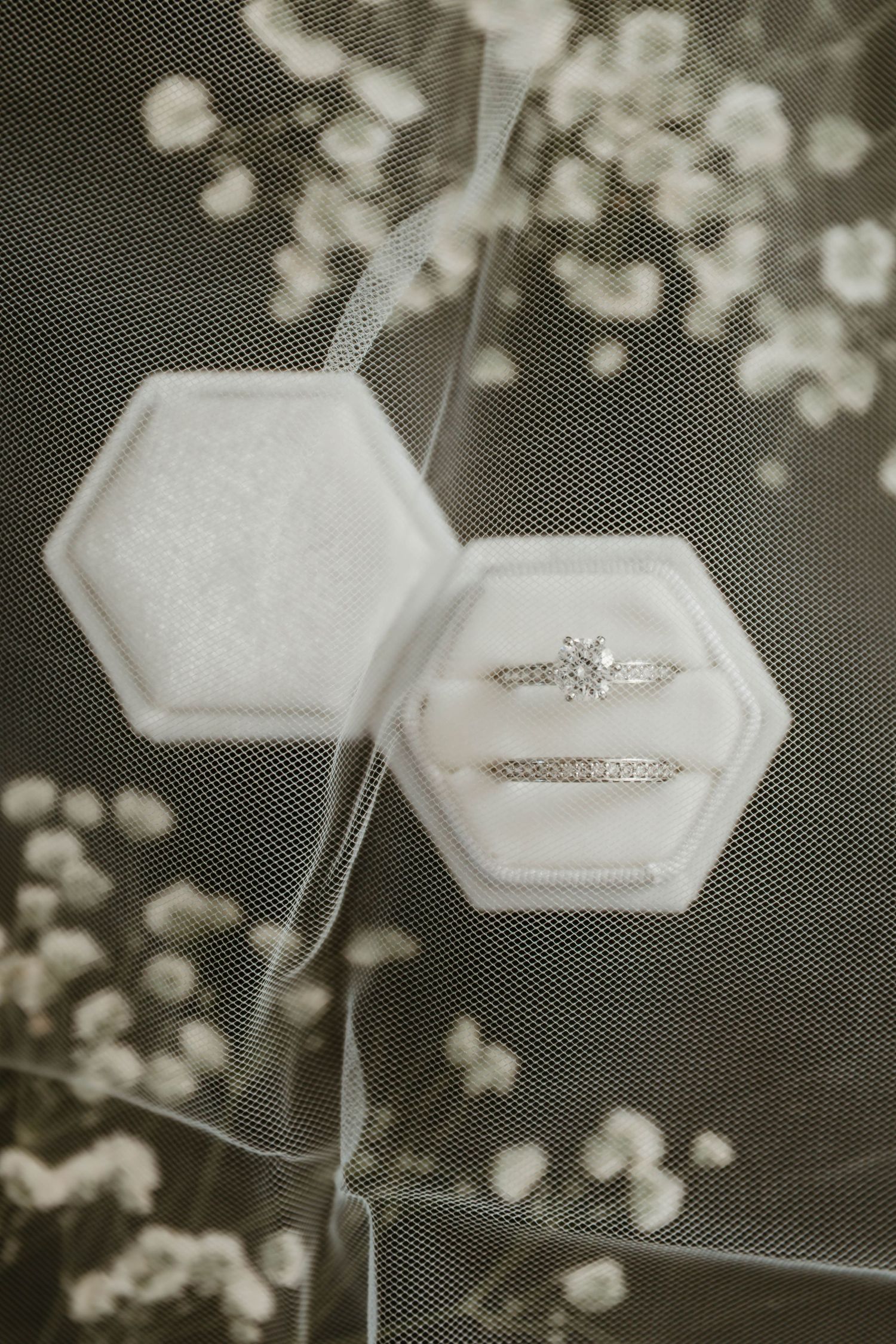 Wedding rings displayed in white hexagonal boxes with soft bokeh background creating an elegant bridal composition.