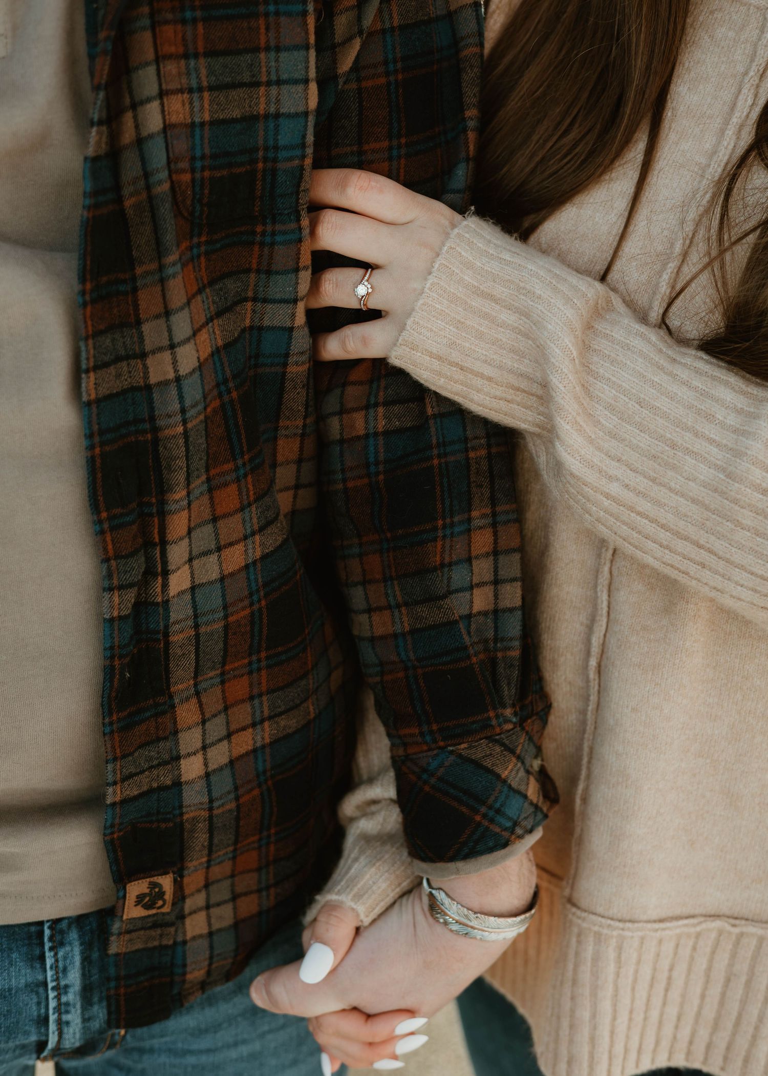 A person wearing a cream sweater and plaid shirt reaches up to adjust something against a dark background.