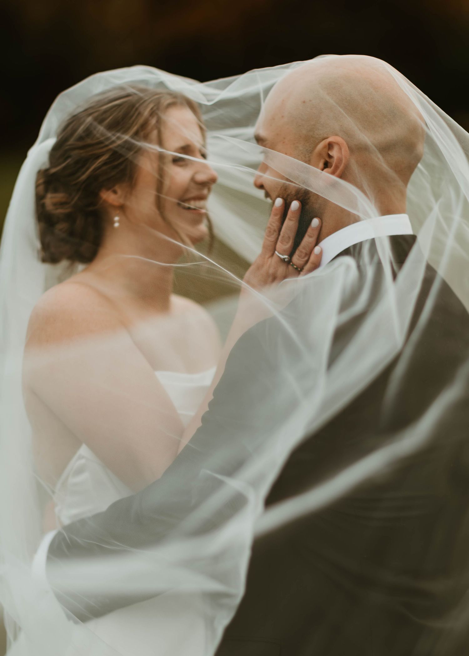 Romantic moment under flowing veil as couple shares intimate moment during wedding portraits.