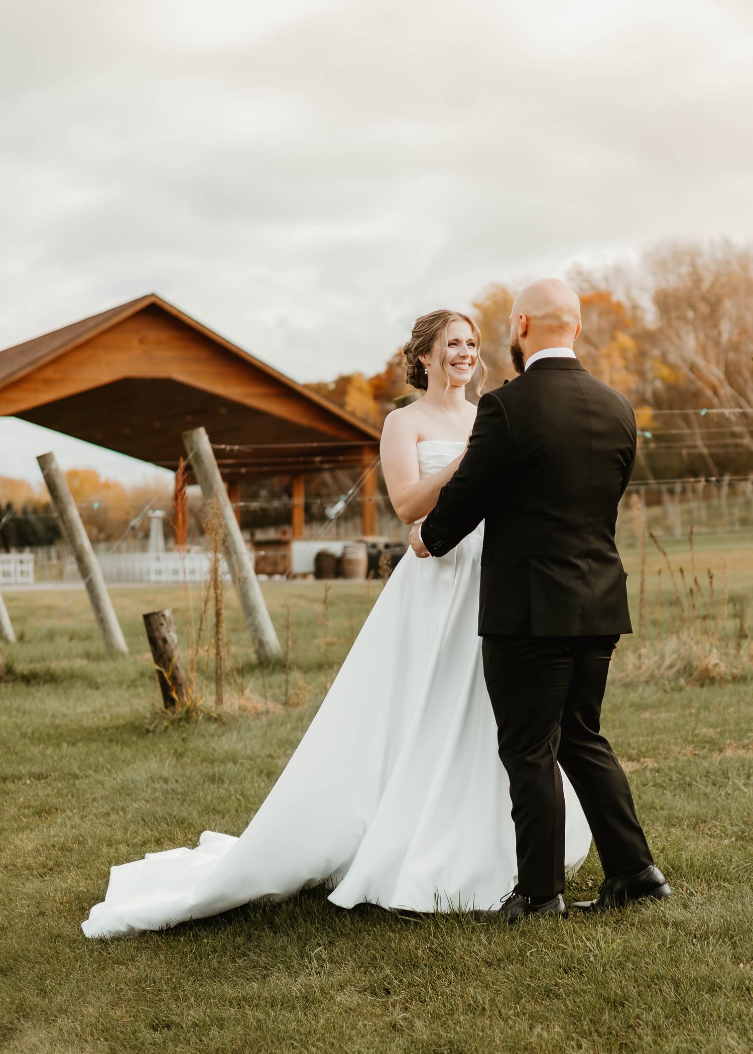 A romantic moment captured between newlyweds dancing outdoors with a rustic barn in the background.