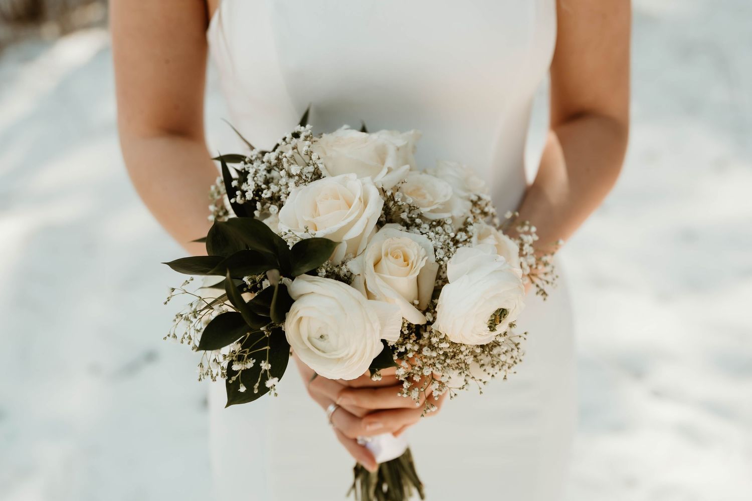 Close-up view of a white bridal bouquet with roses and baby's breath against a light background.