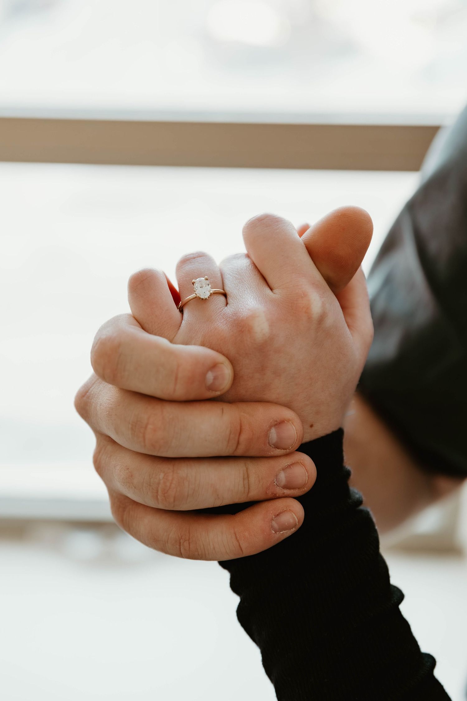 Close-up of hands clasped together showing a sparkling engagement ring.