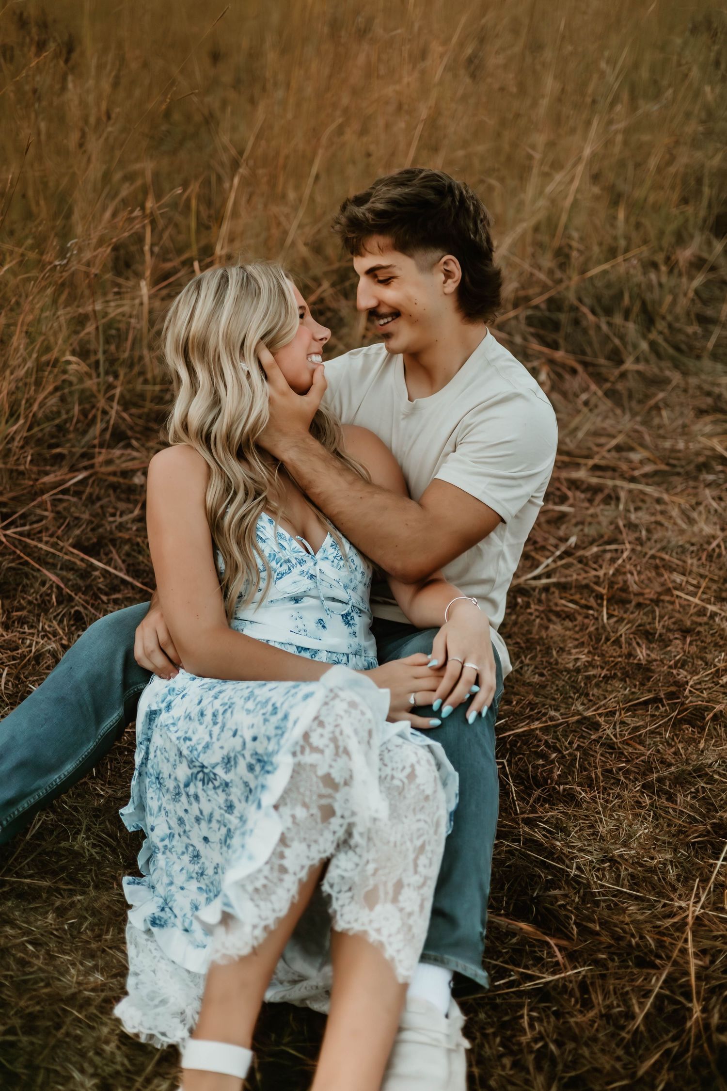 A romantic couple sits in a field of tall grass, sharing an intimate moment in warm autumn light.