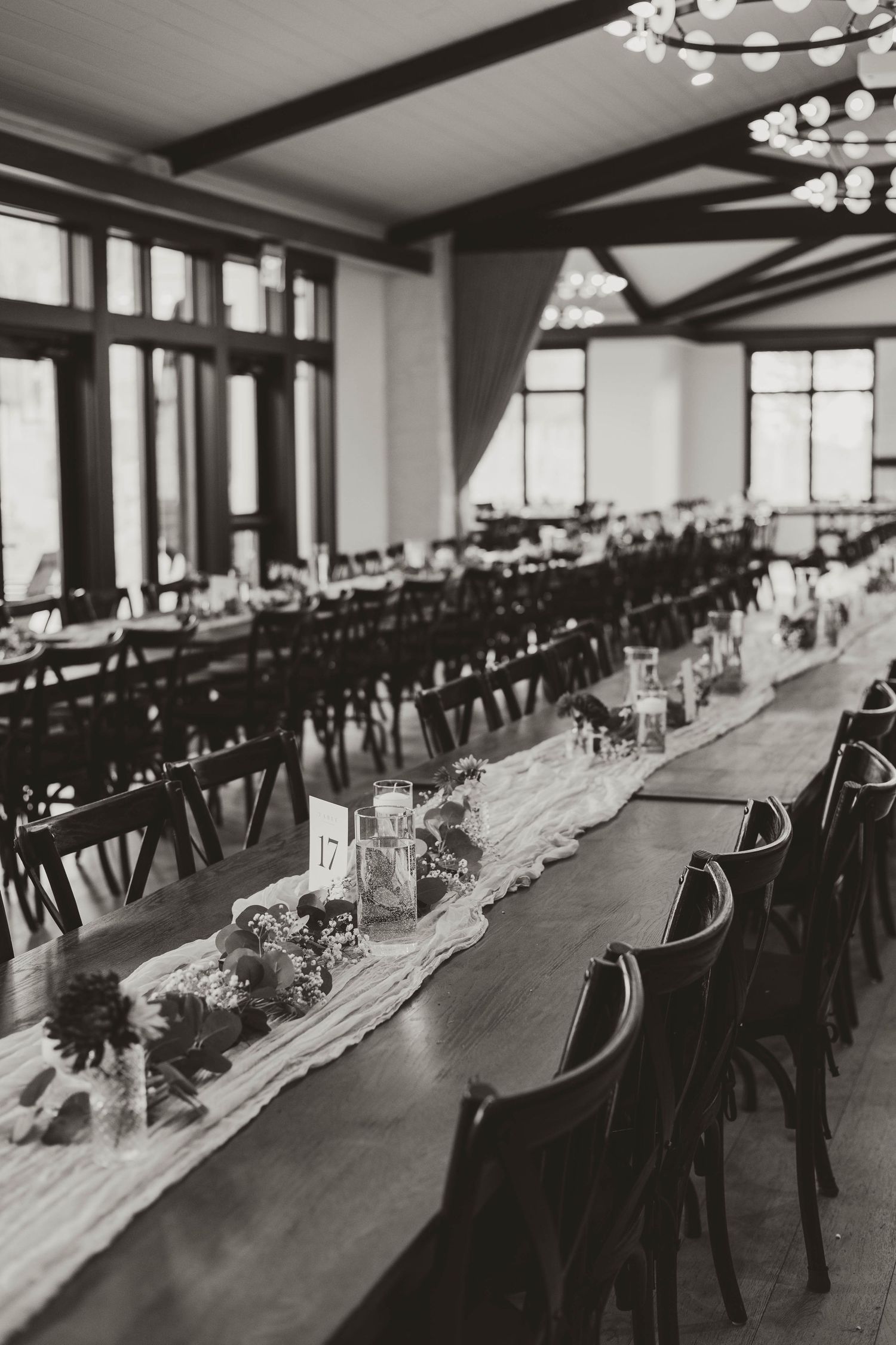 Elegant wedding reception hall with long tables, dark chairs and chandelier lighting.