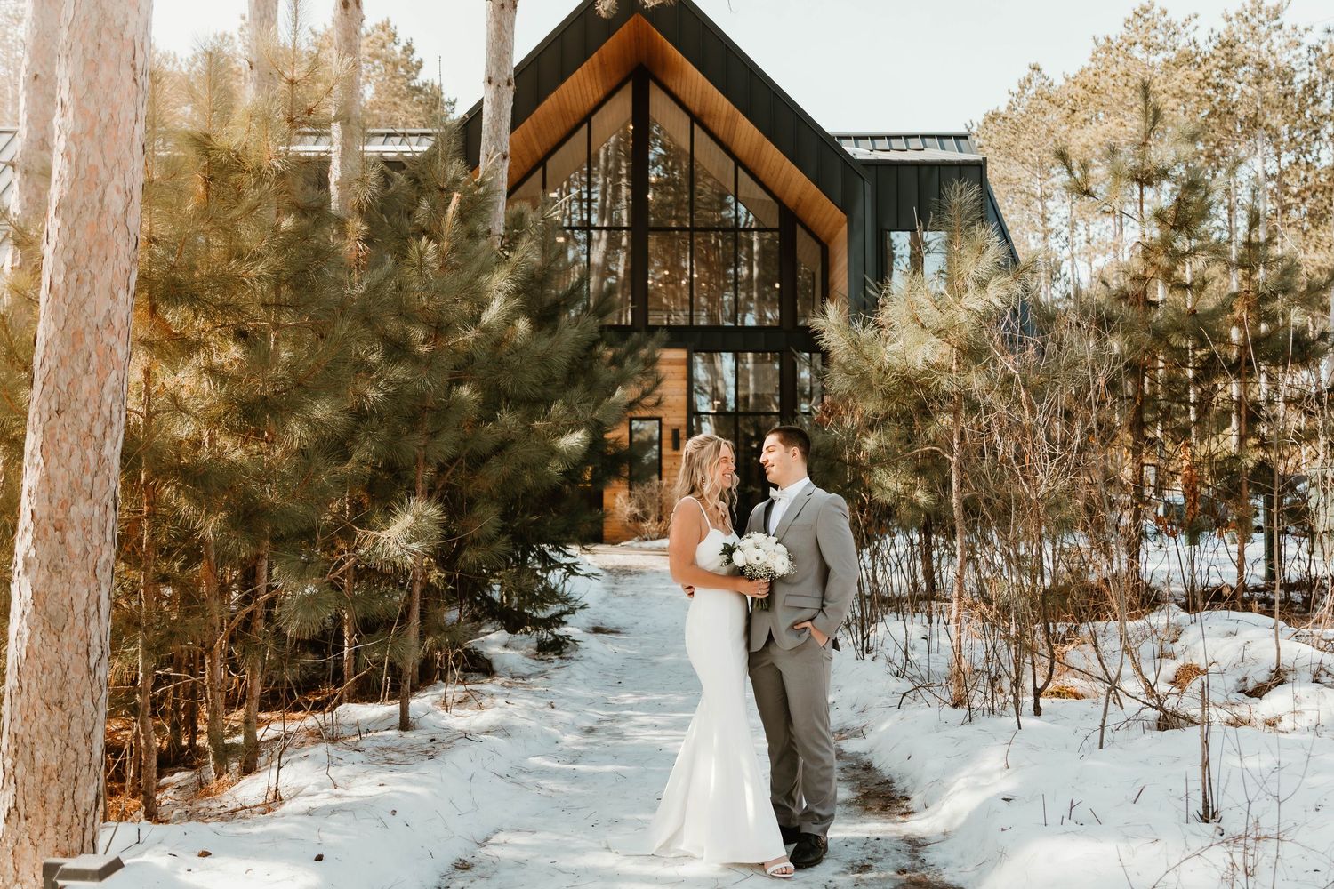 Snow-covered winter wedding venue with wooden A-frame chapel among pine trees.