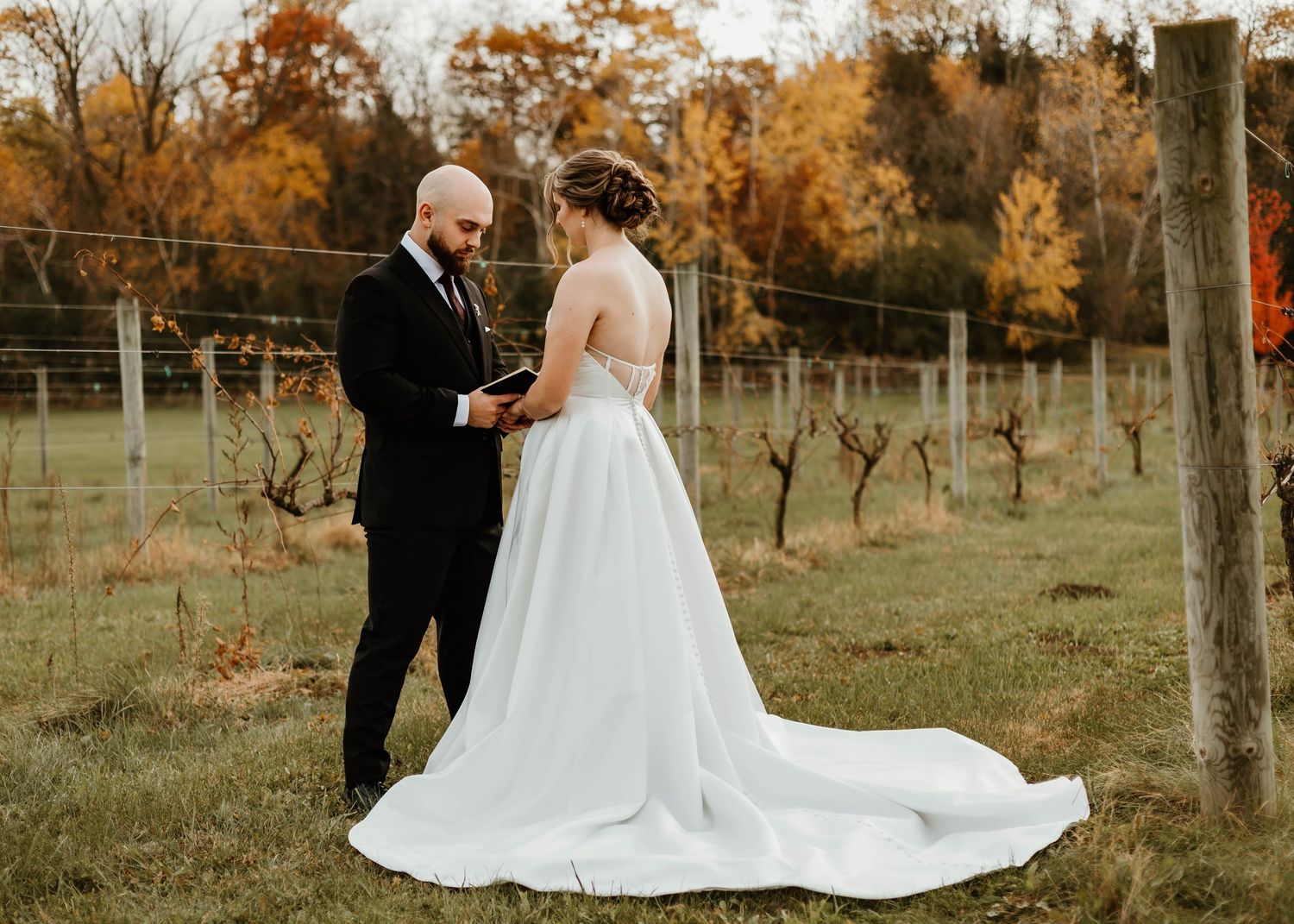 Bride in flowing white gown walks through autumn vineyard with golden foliage in background.