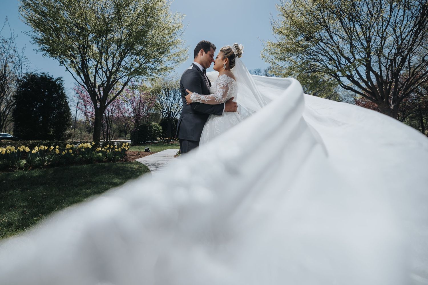 Wedding couple embracing on a sunny day with dramatic flowing dress.