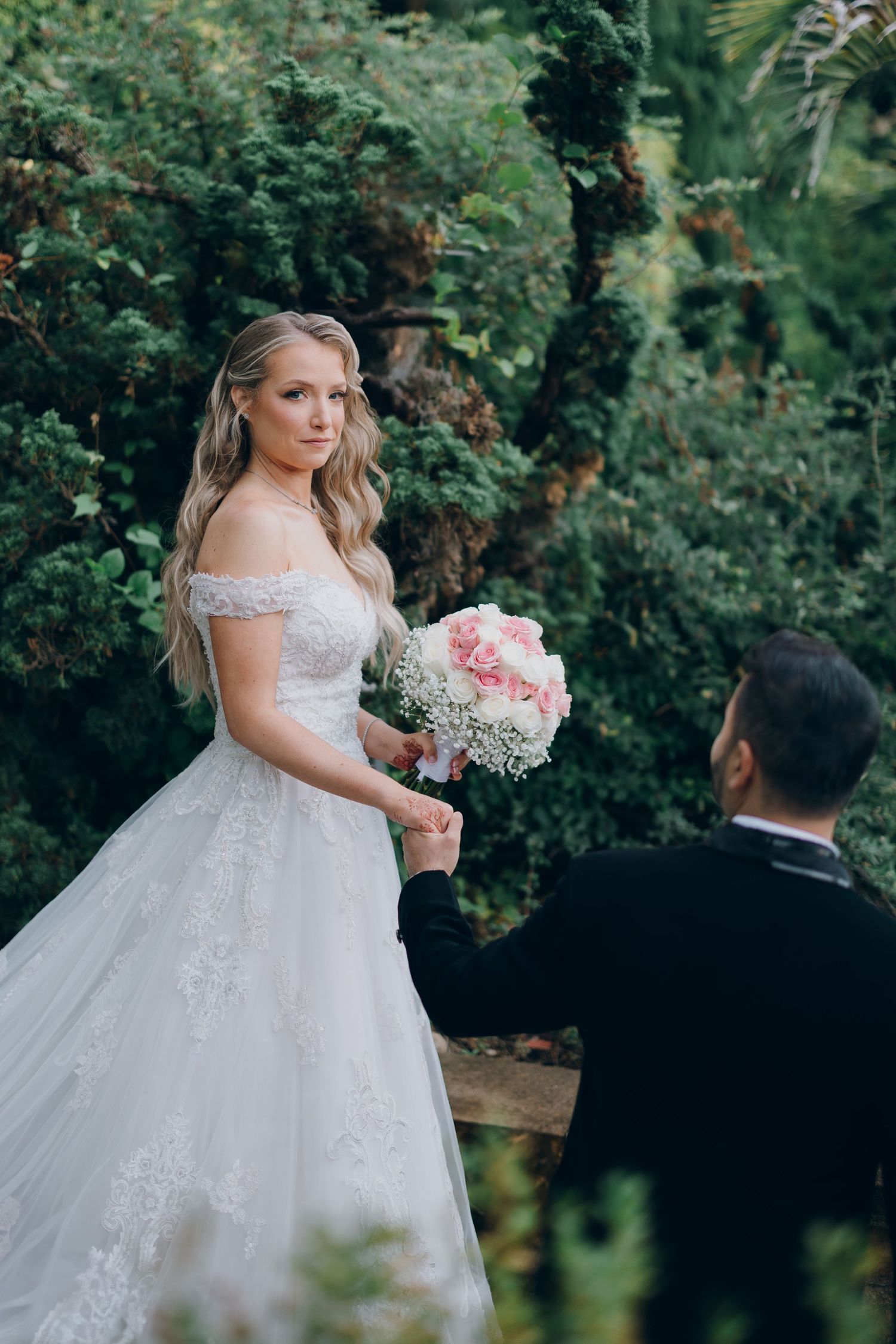 Wedding couple posing in lush garden setting with pink bouquet.