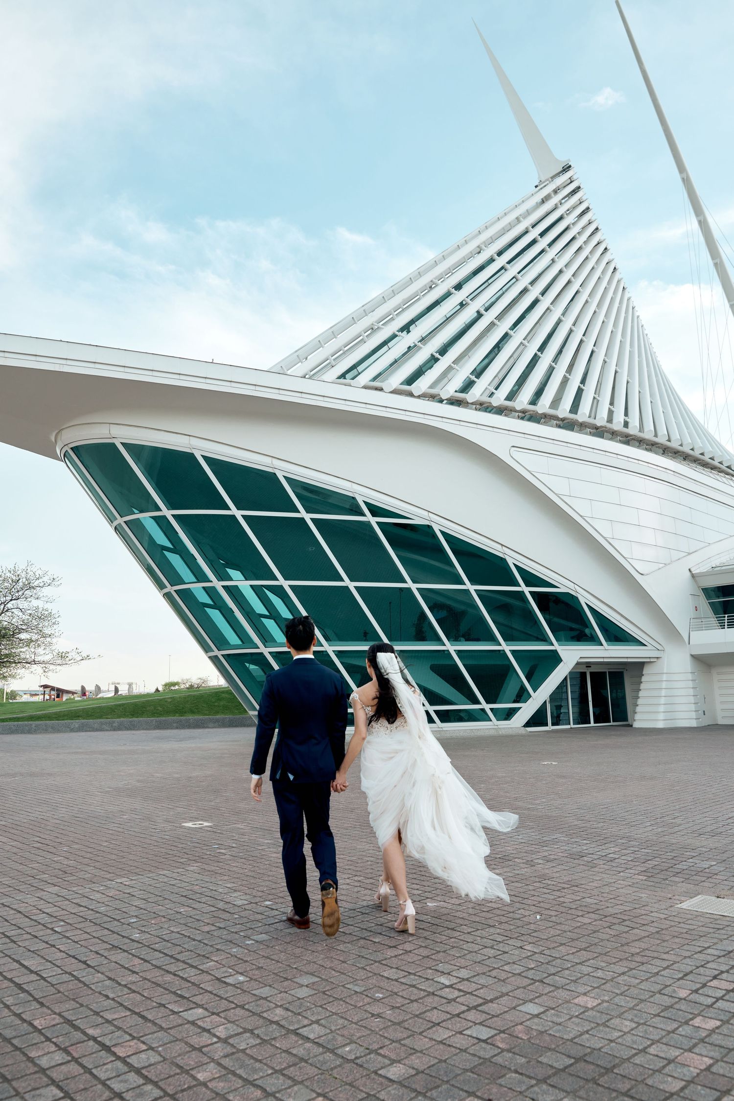 A couple walks towards modern architectural building with dramatic angular white roof.