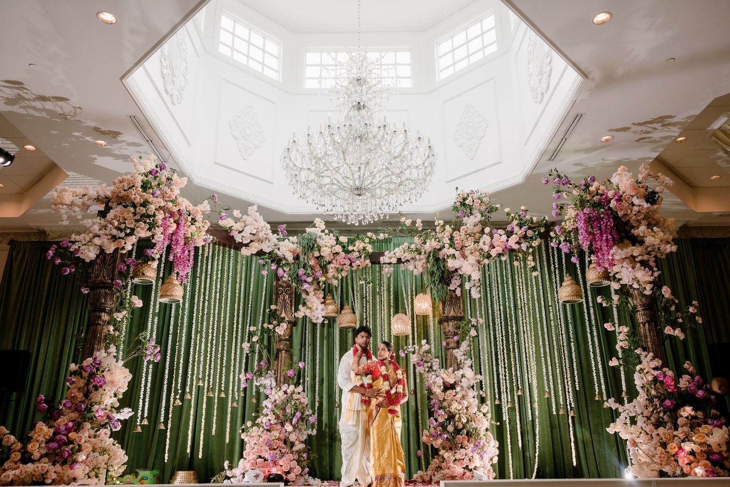 Elegant wedding venue with crystal chandelier and pink floral arch decorations.