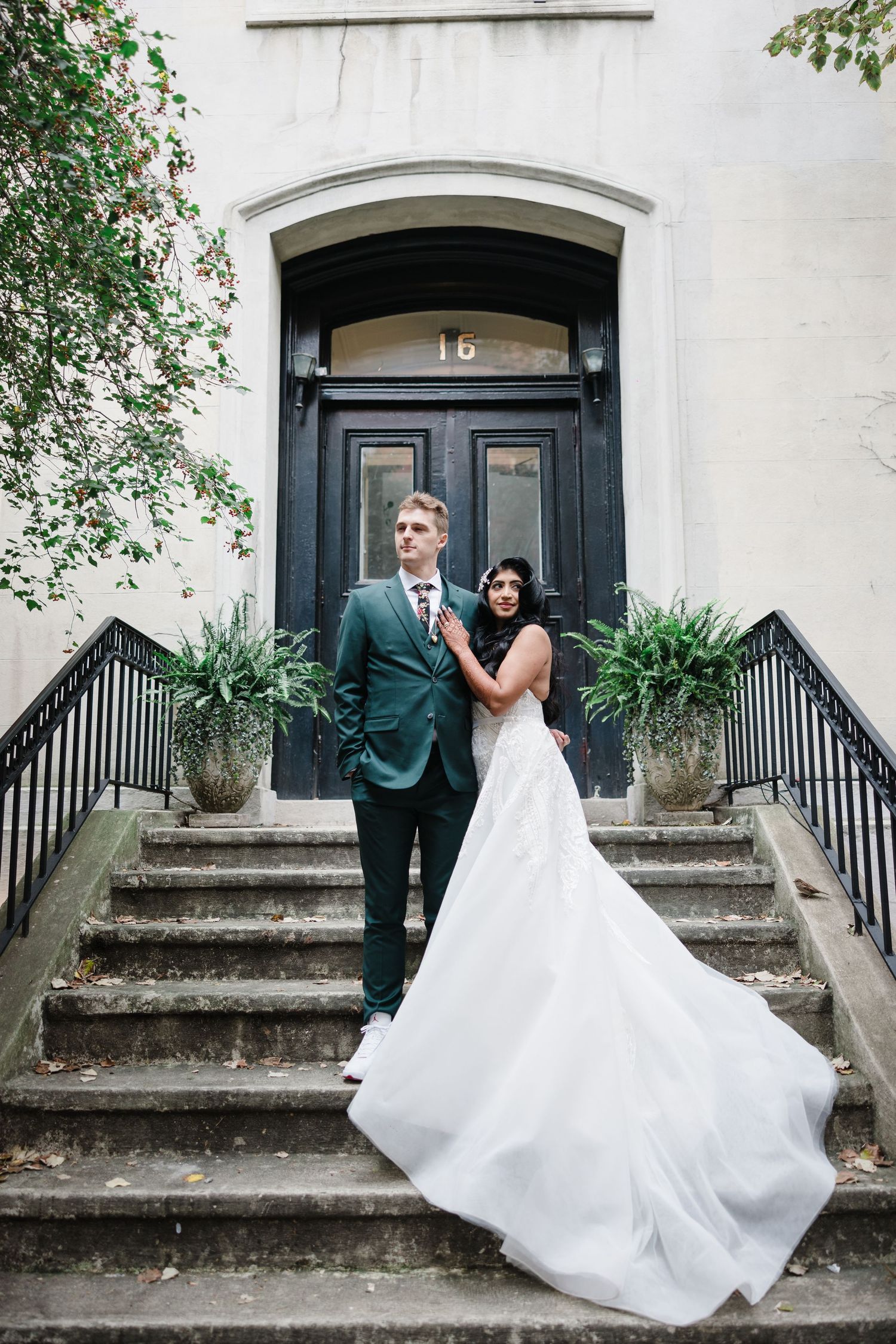A couple poses on historic building steps with a flowing white wedding dress.