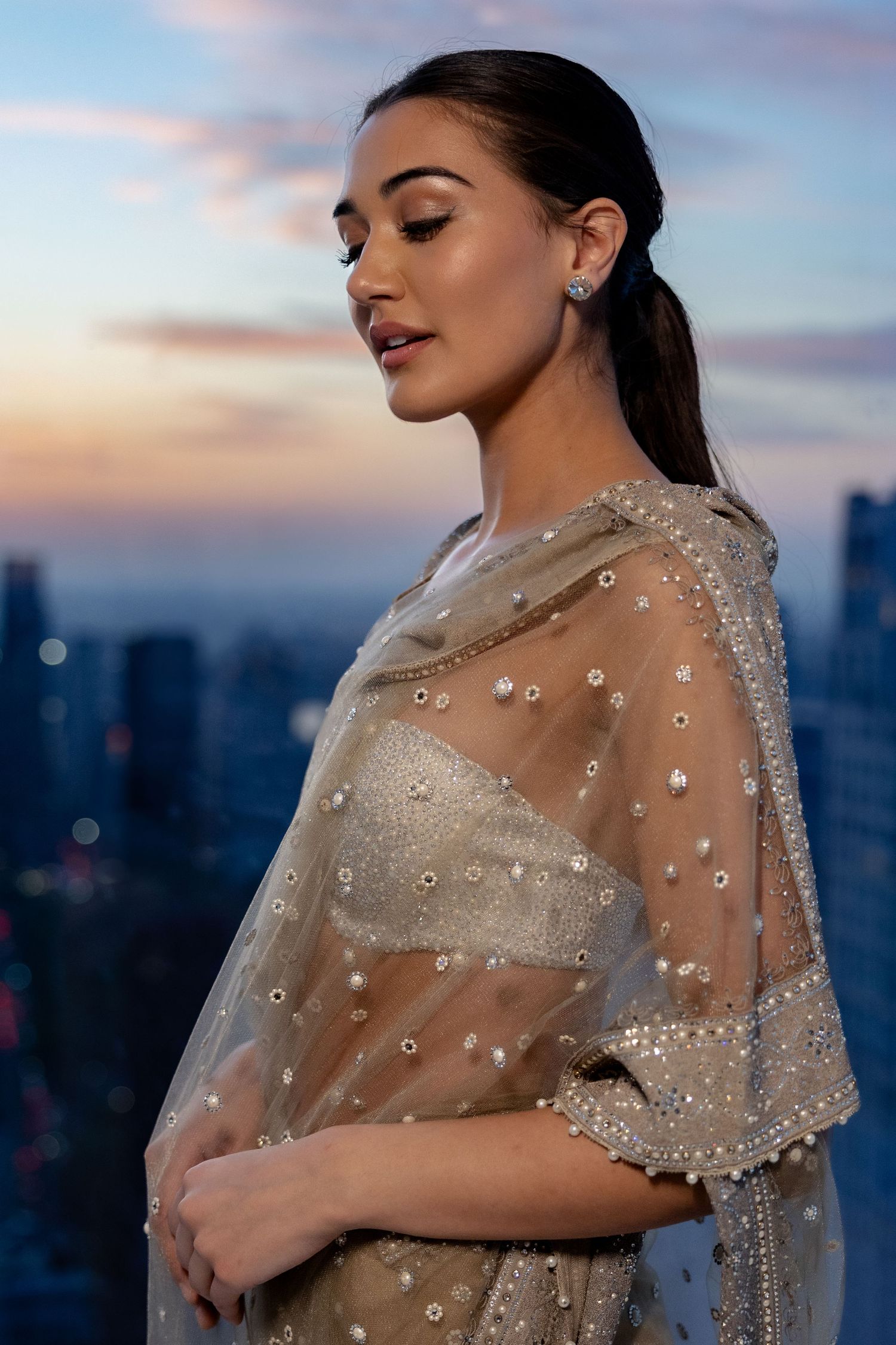 A glamorous evening portrait features sparkling sheer fabric against a twilight city backdrop.