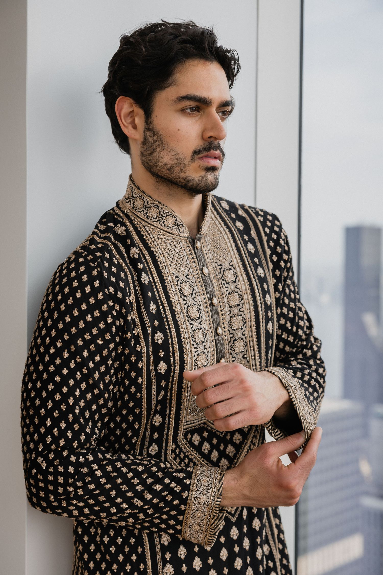 A detailed shot of traditional South Asian formal wear with intricate gold embroidery on black fabric.