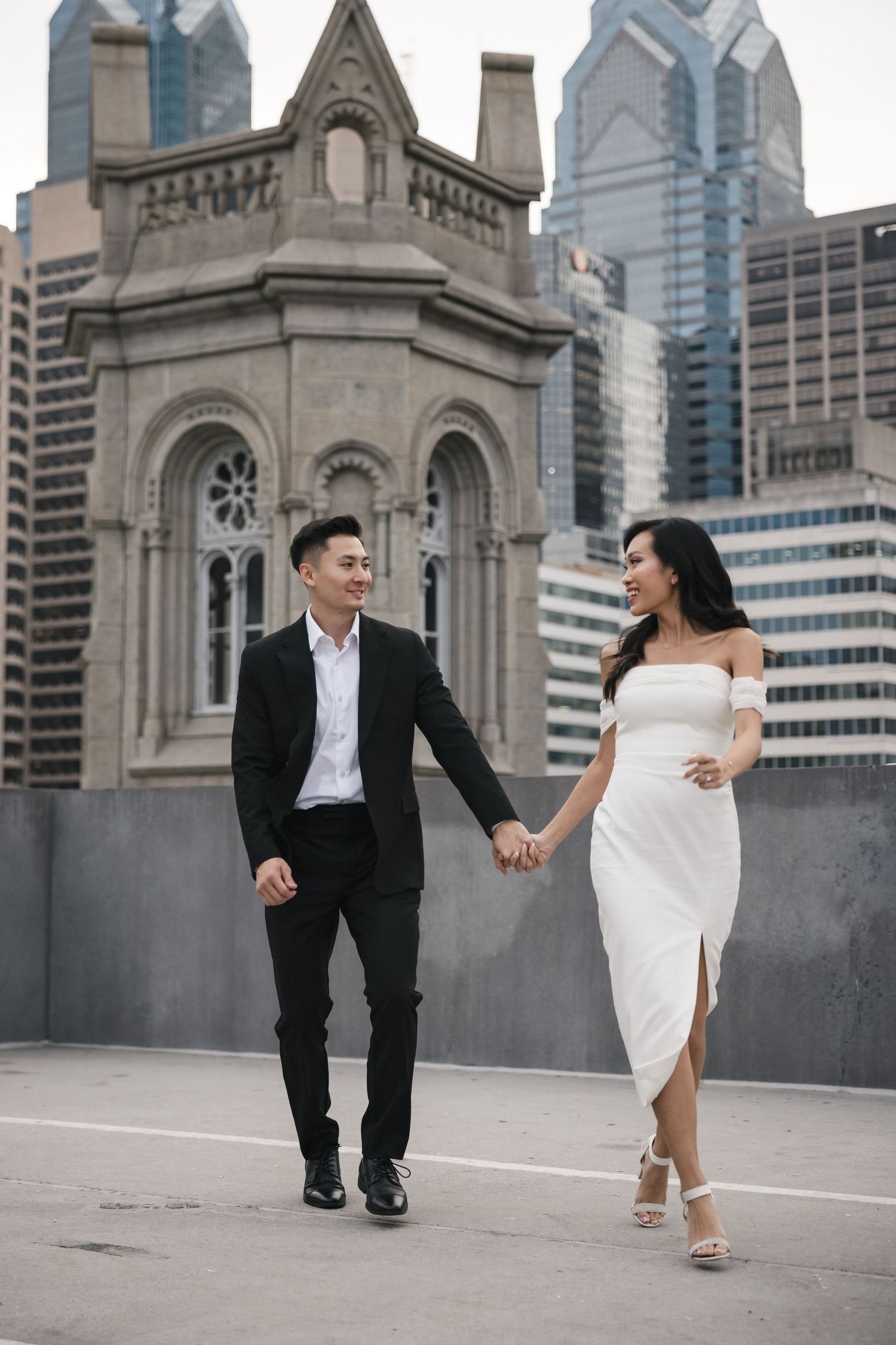 Couple in formal attire running playfully on urban rooftop with church architecture.
