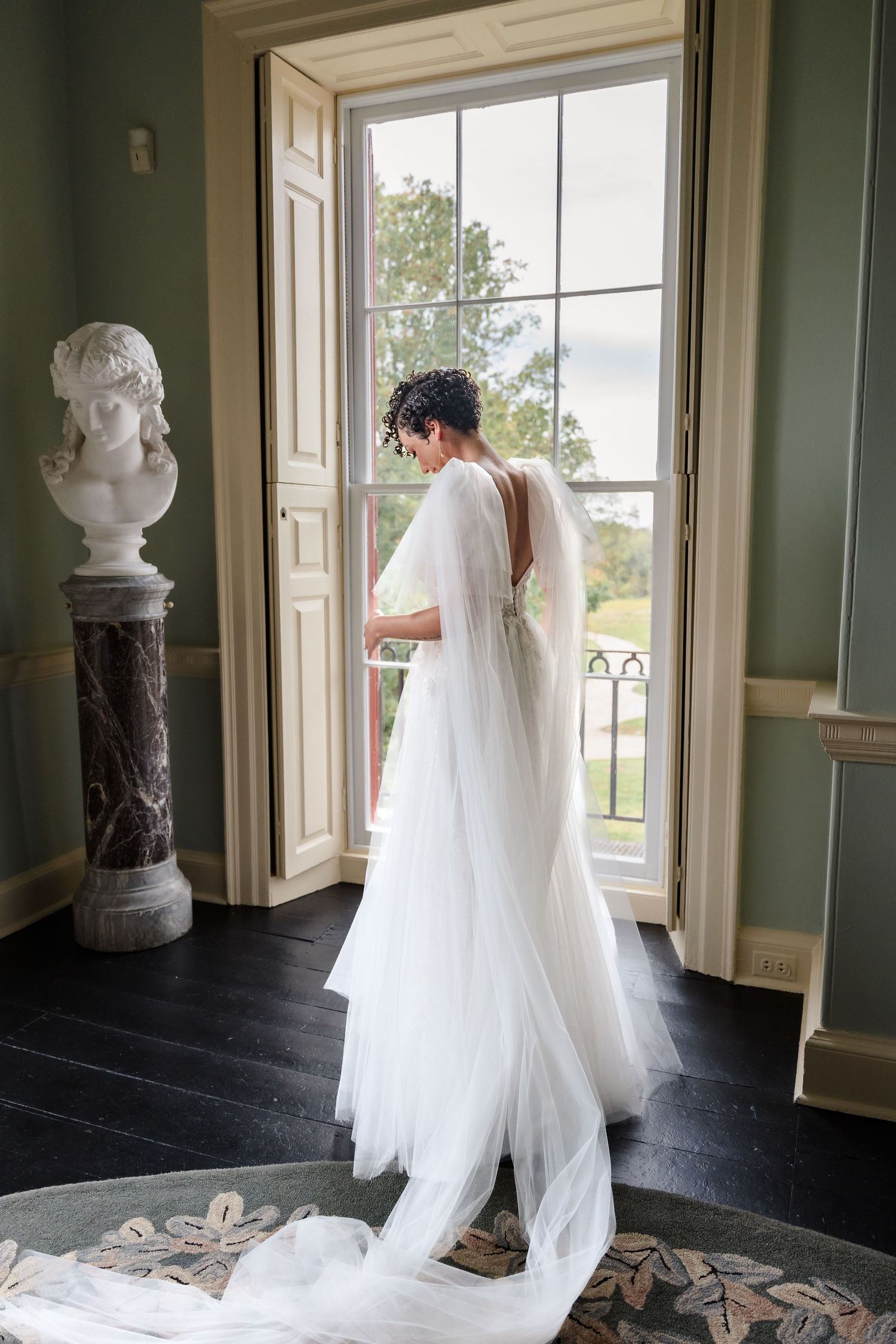 Ethereal wedding dress with flowing train captured in natural light by historic windows.