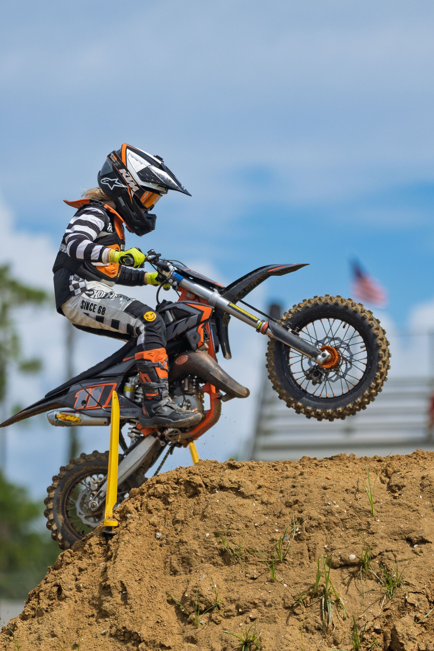 Dirt bike flying over a dirt mound against blue sky.
